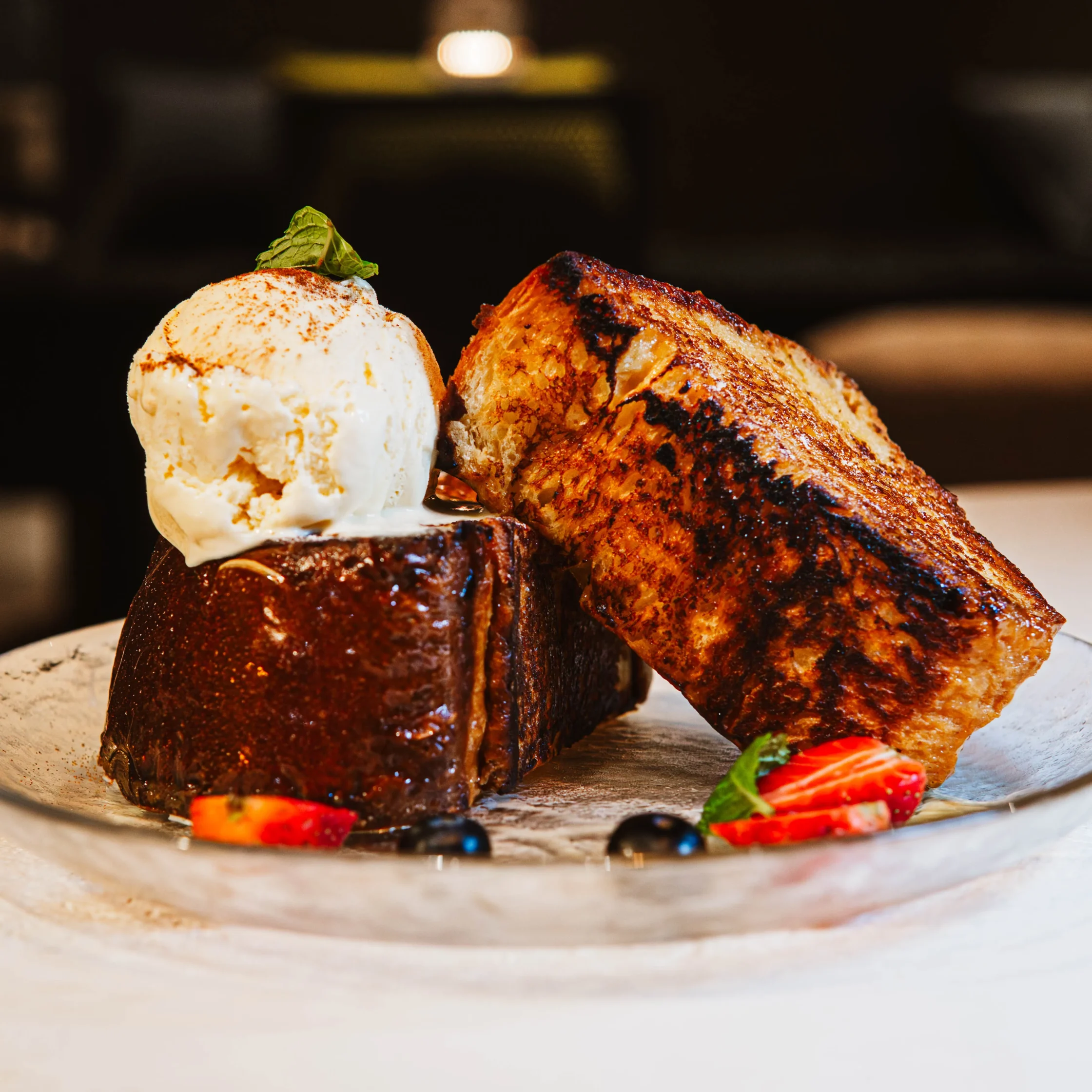 Caramelized brioche bread plated with strawberries and topped with vanilla ice cream