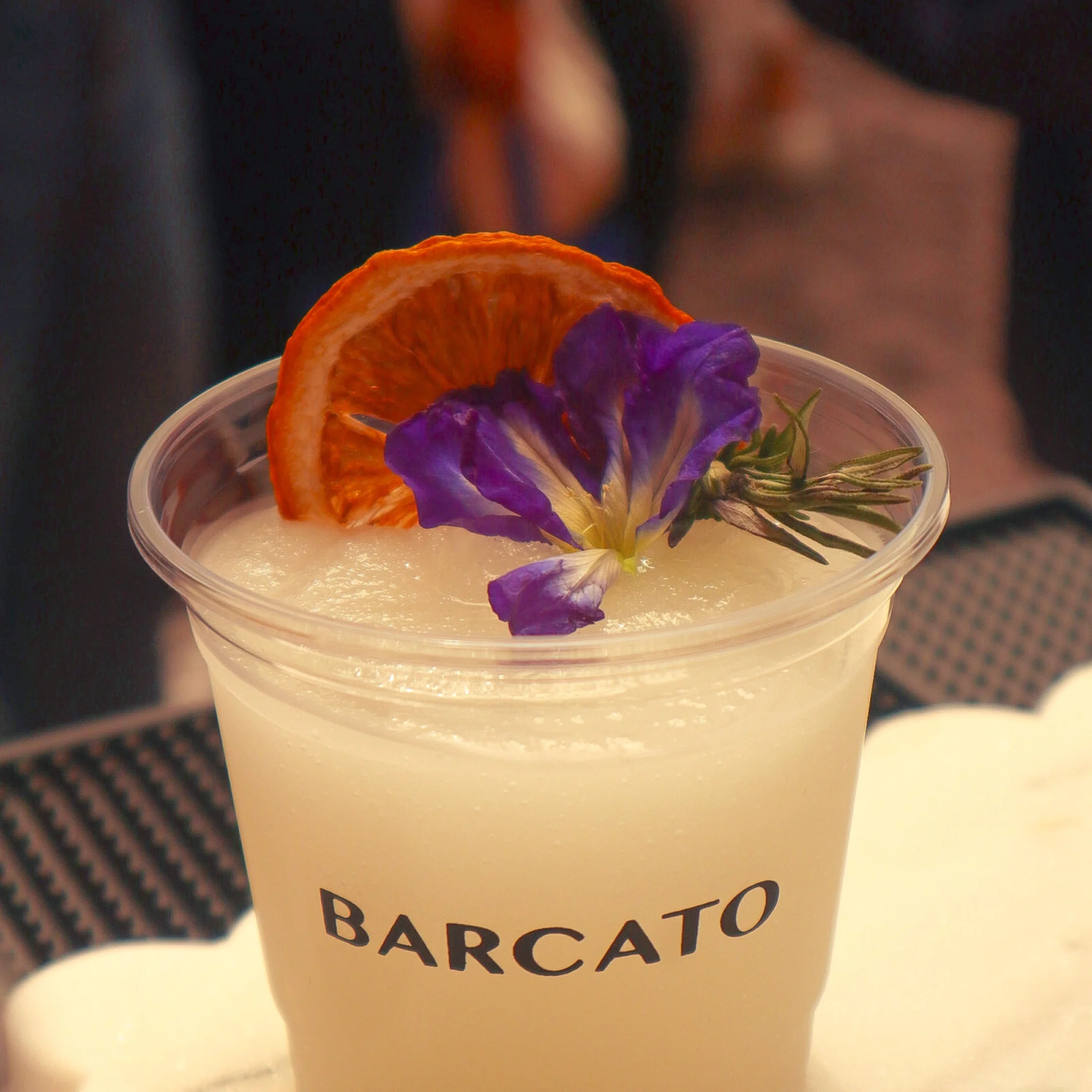 White cocktail with orange slice garnish and purple flower