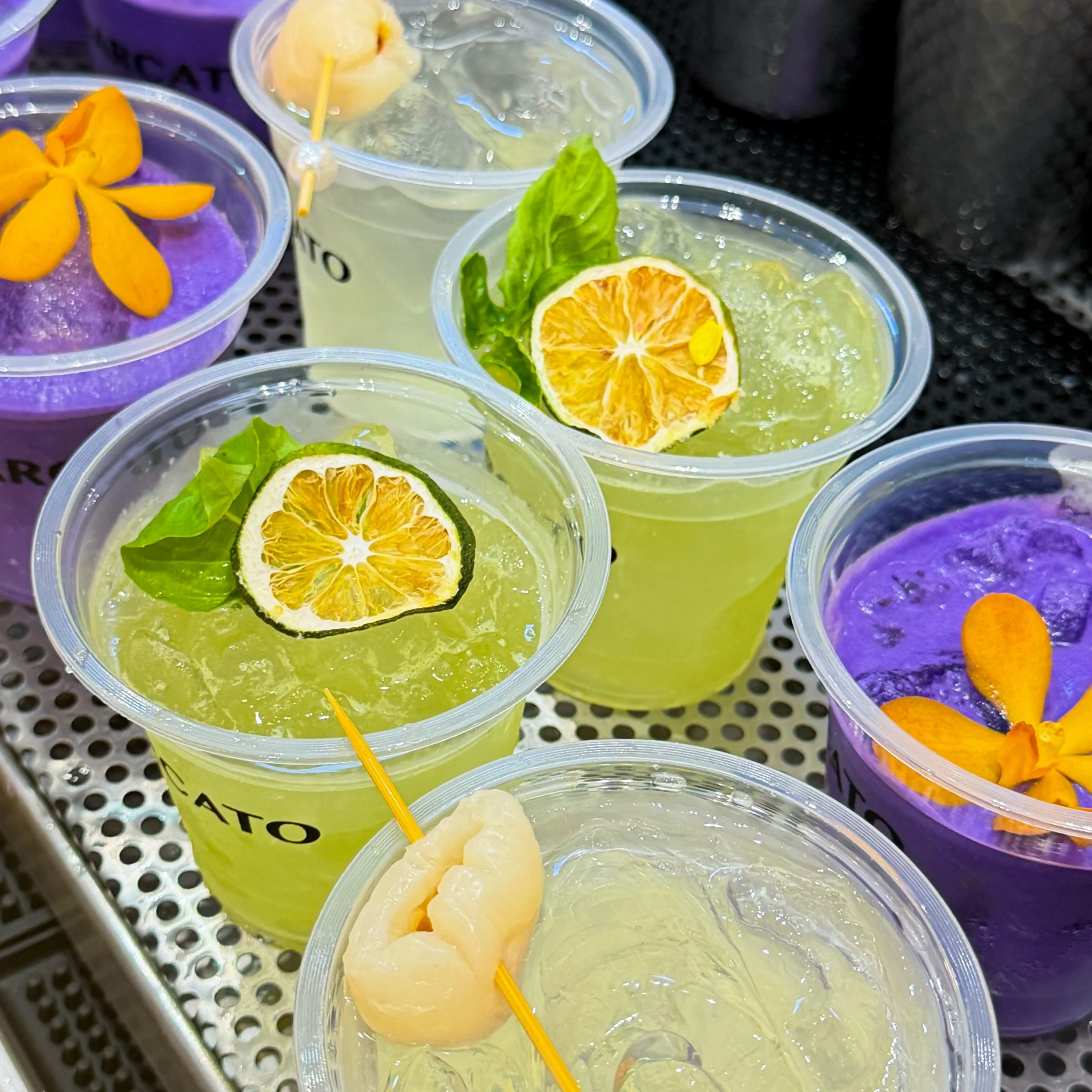 Purple, green, and clear cocktails in plastic cups with floral garnish