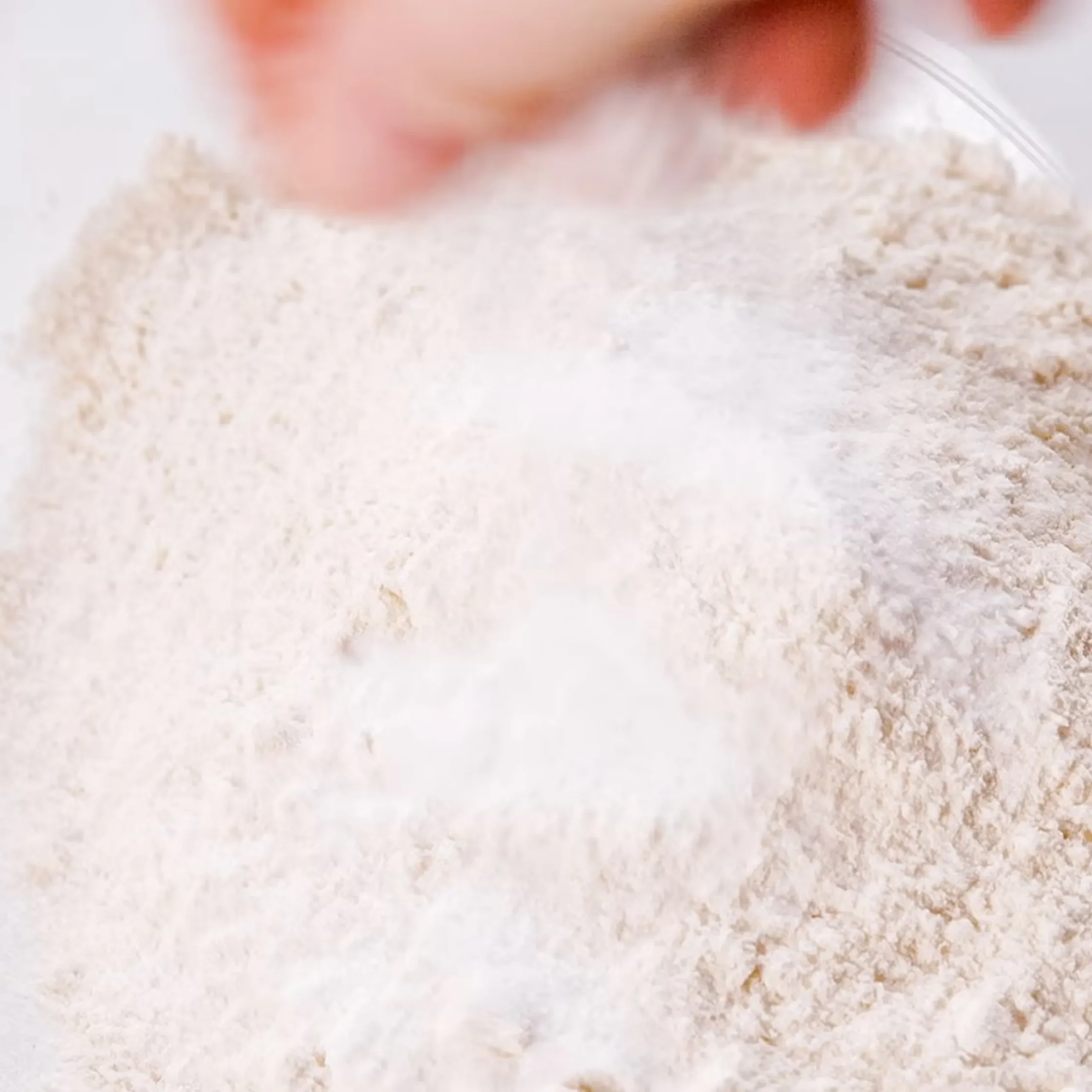 Close-up of white flour scattered on a surface with a whisk nearby.