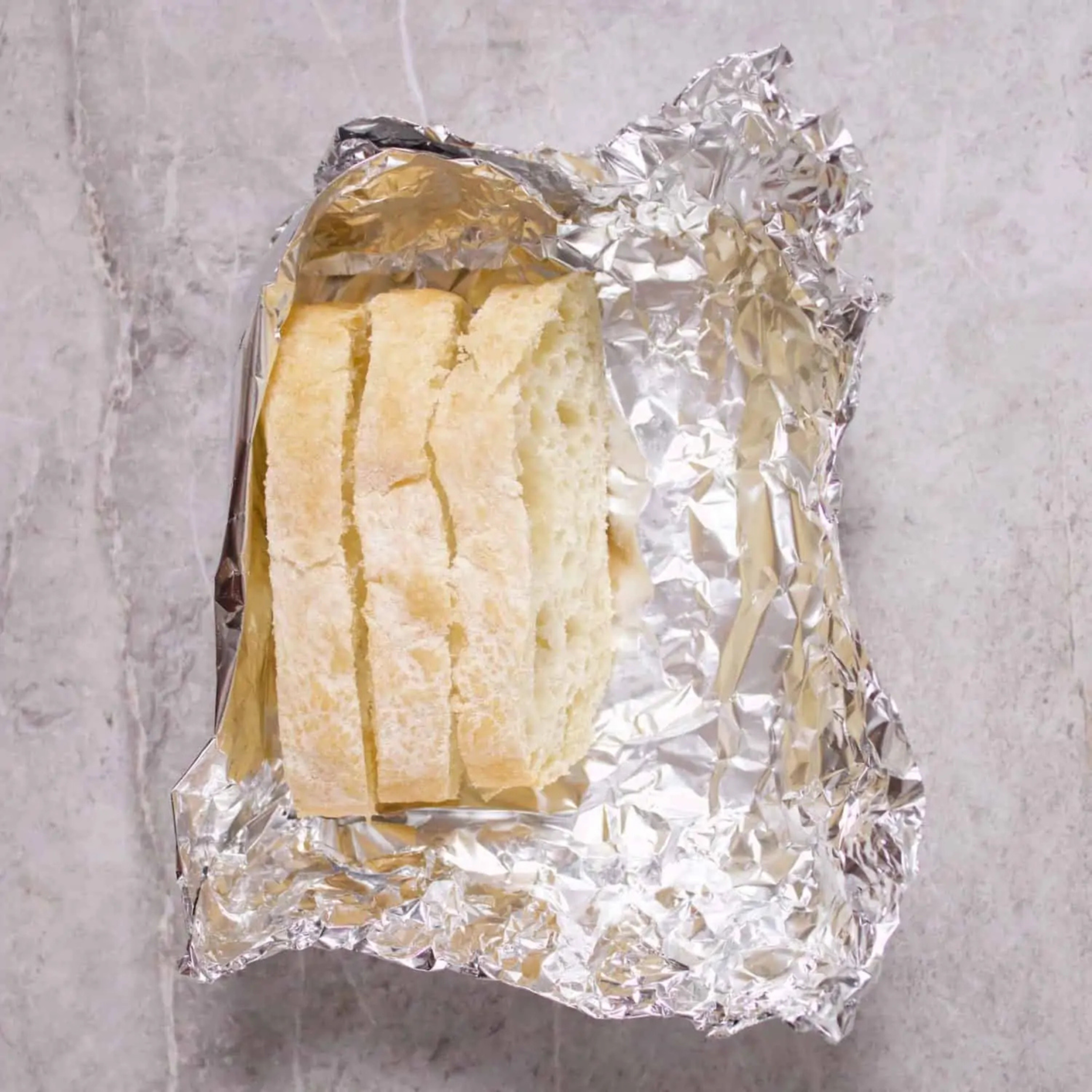 Loaf of sliced bread partially unwrapped from crinkled aluminum foil on a gray countertop.