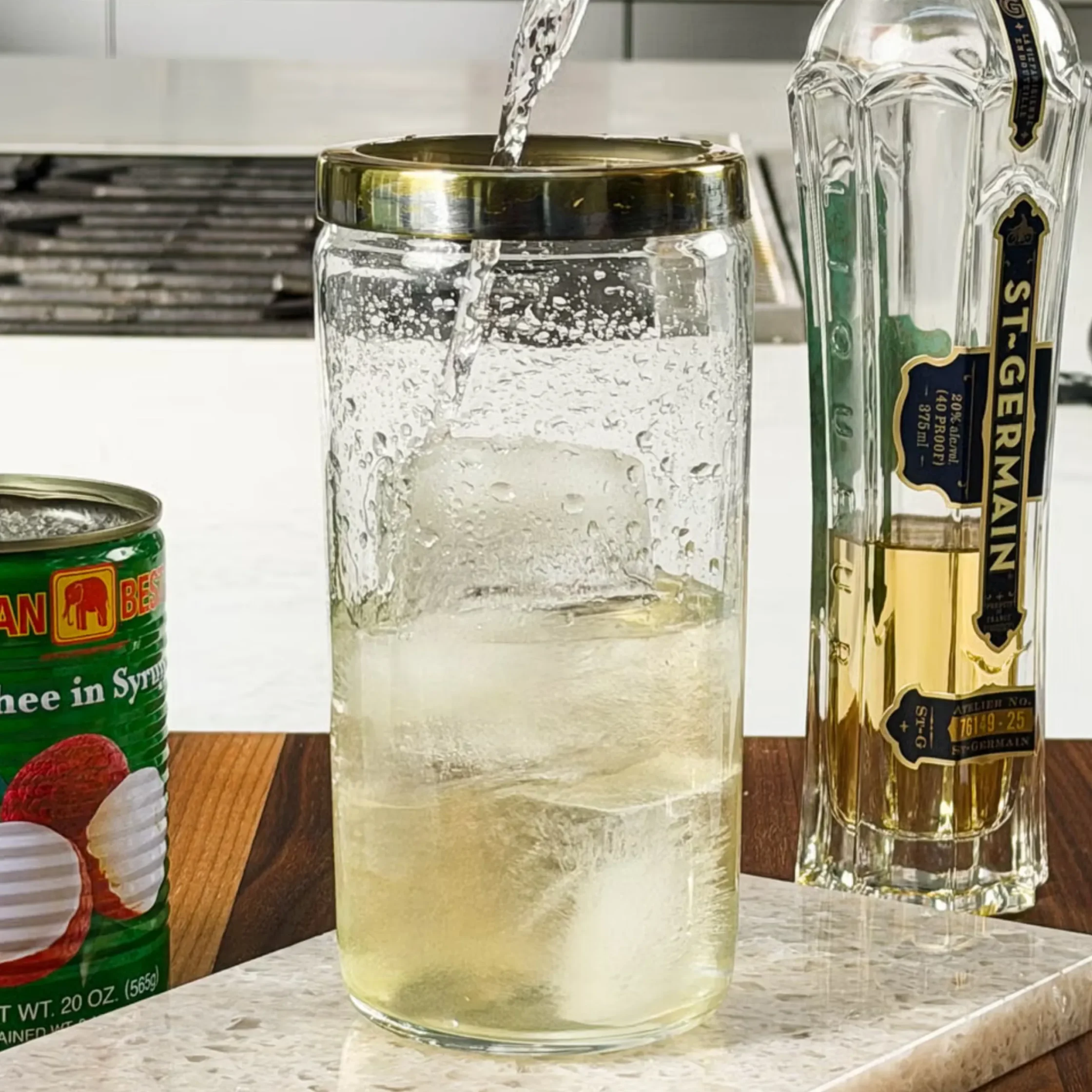 Frosted glass being filled with a cold drink; gin bottle on the right and a can on the left.