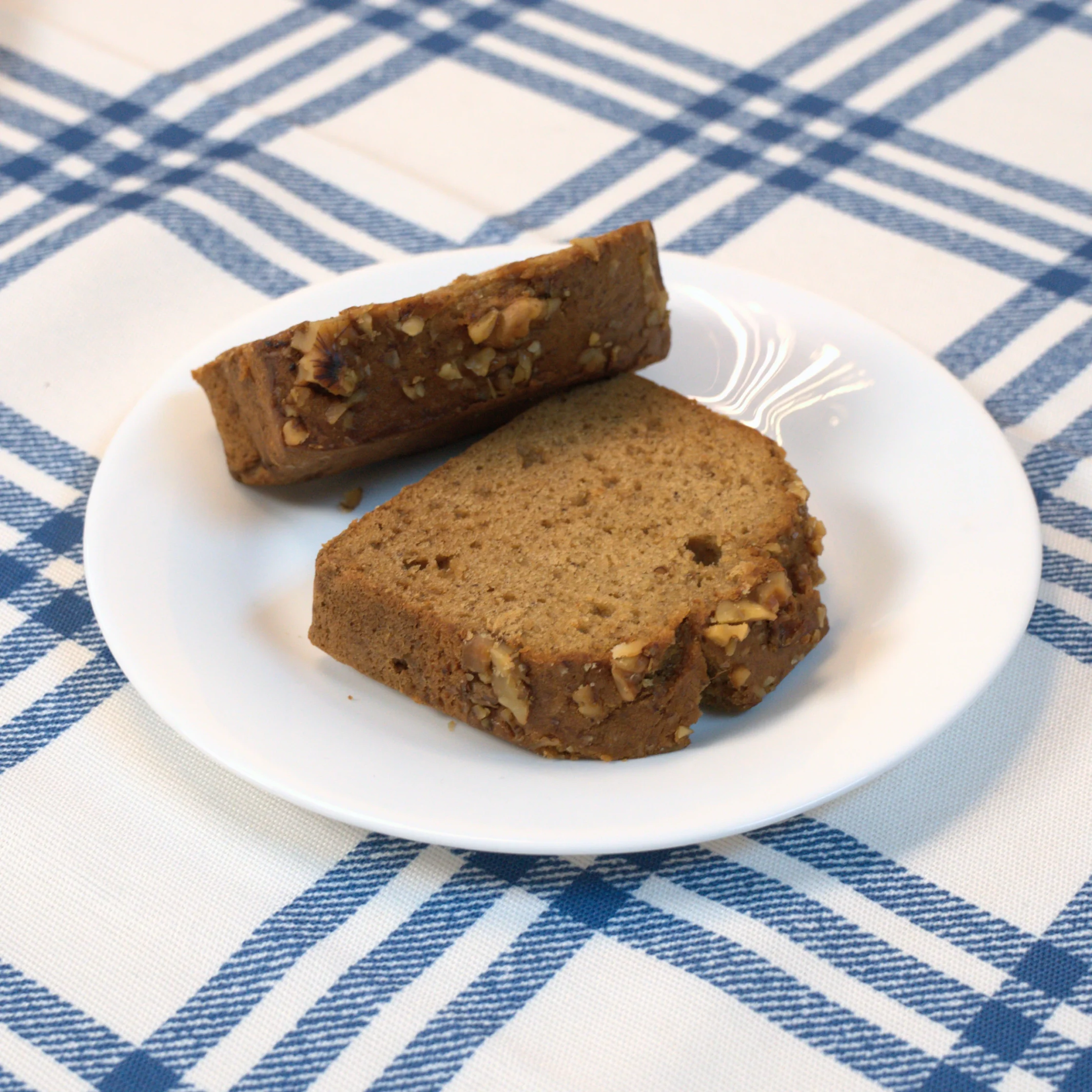 Slices of nut-tleck loaf cake on a white plate, resting on a blue-and-white checkered tablecloth.