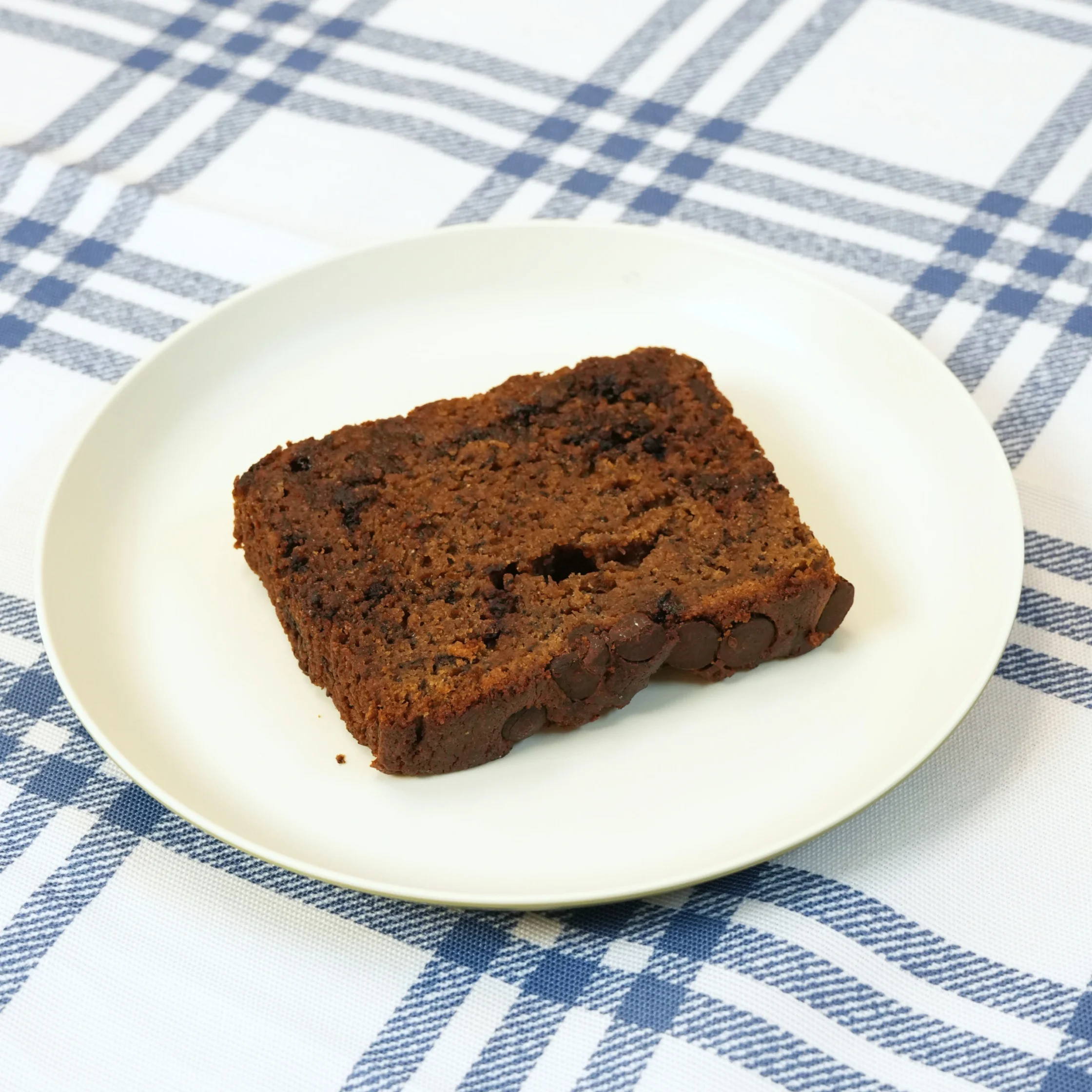 A thick, fudgy brownie slice on a white plate atop a blue plaid tablecloth.