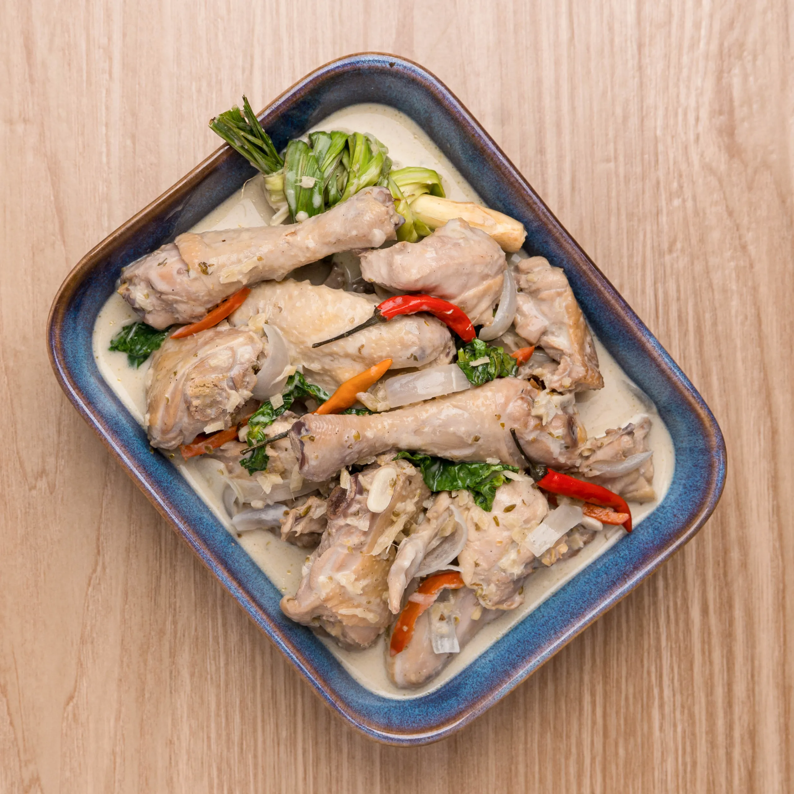 Sliced chicken with peppers, onions and greens in a light sauce on a blue ceramic plate