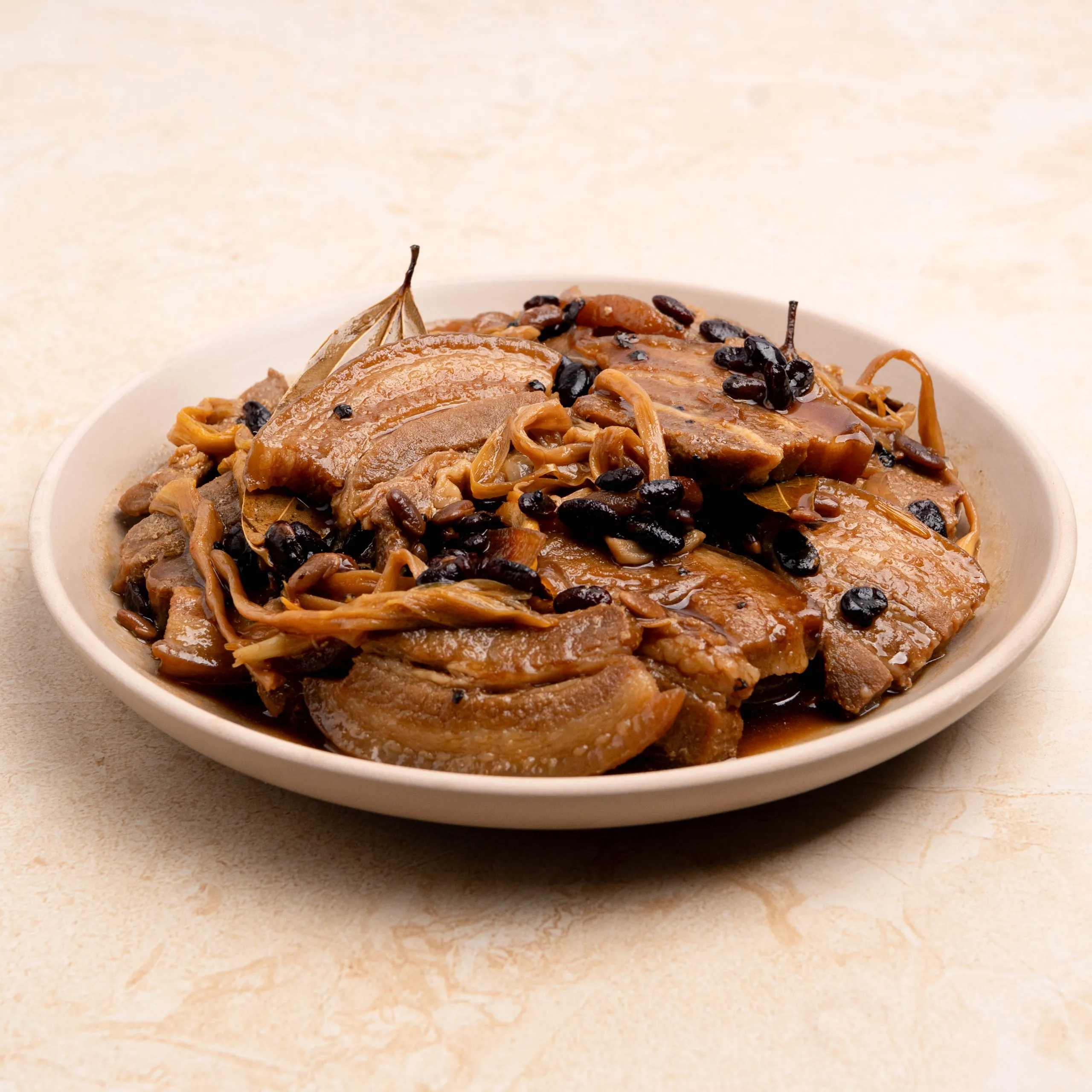 Plate of braised beef with caramelized onions and dark raisins on top, served in a white bowl.