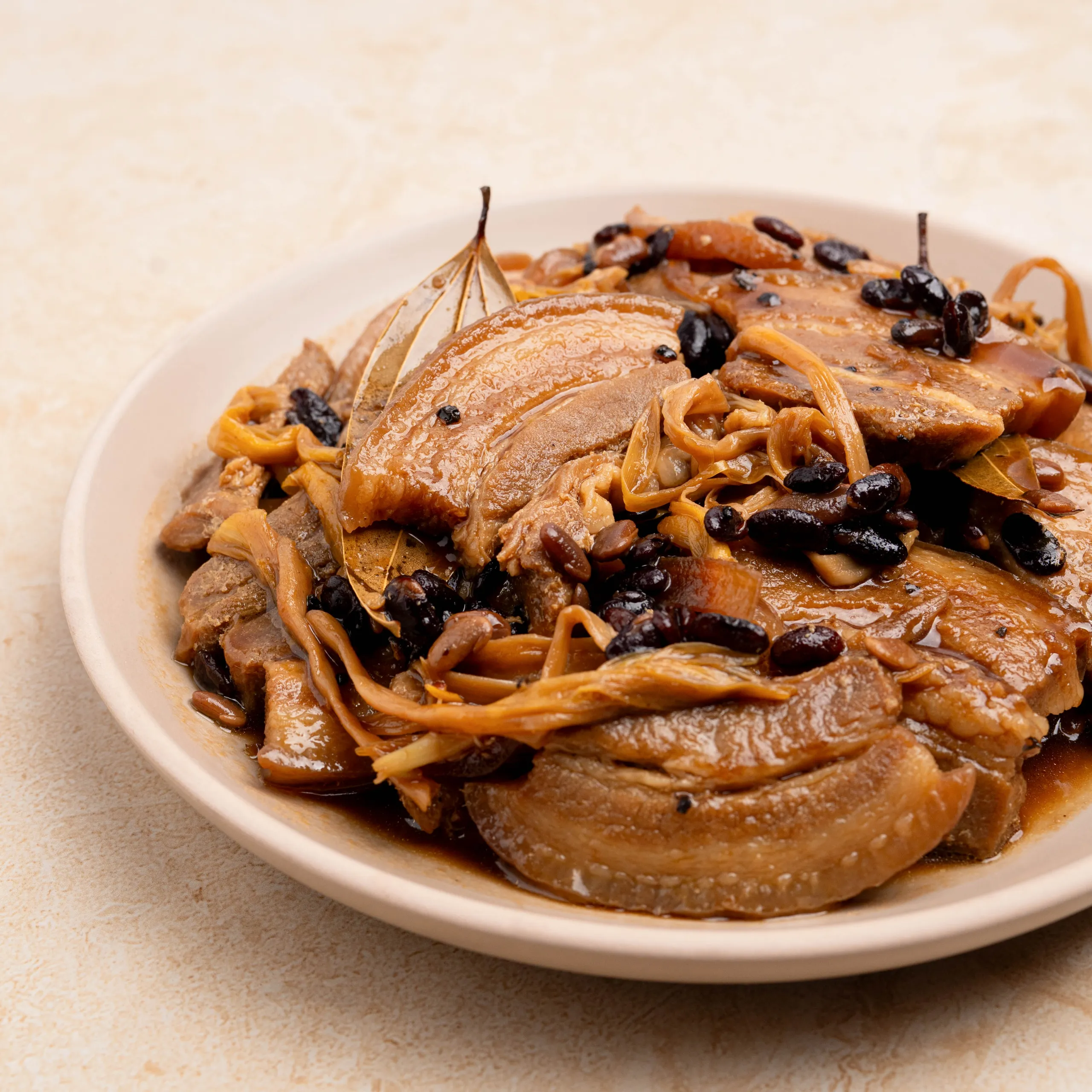 Sliced braised beef in brown gravy with onions and black beans on a white plate.
