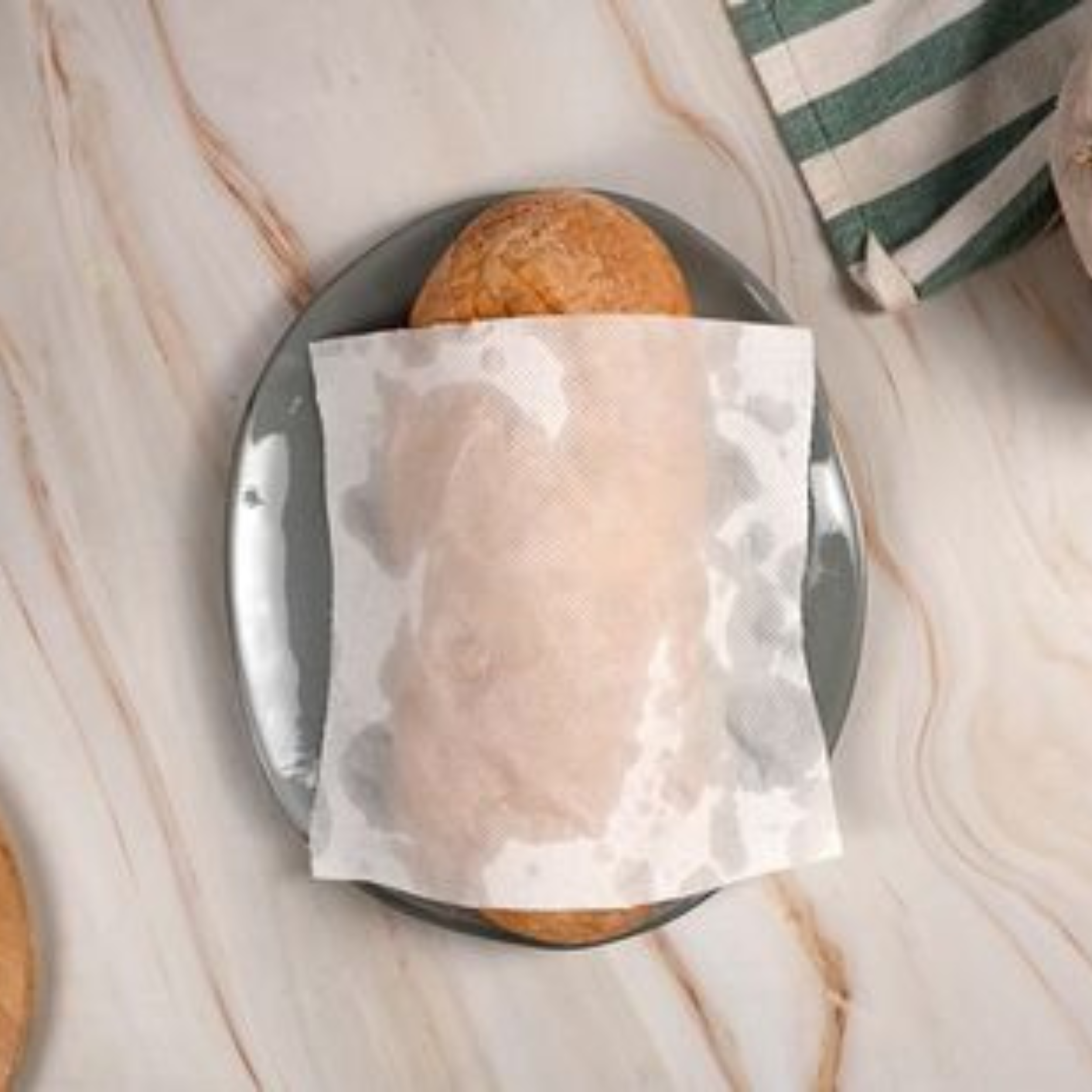 Round, crusty bread roll on a plate with a napkin, set on a light wooden table
