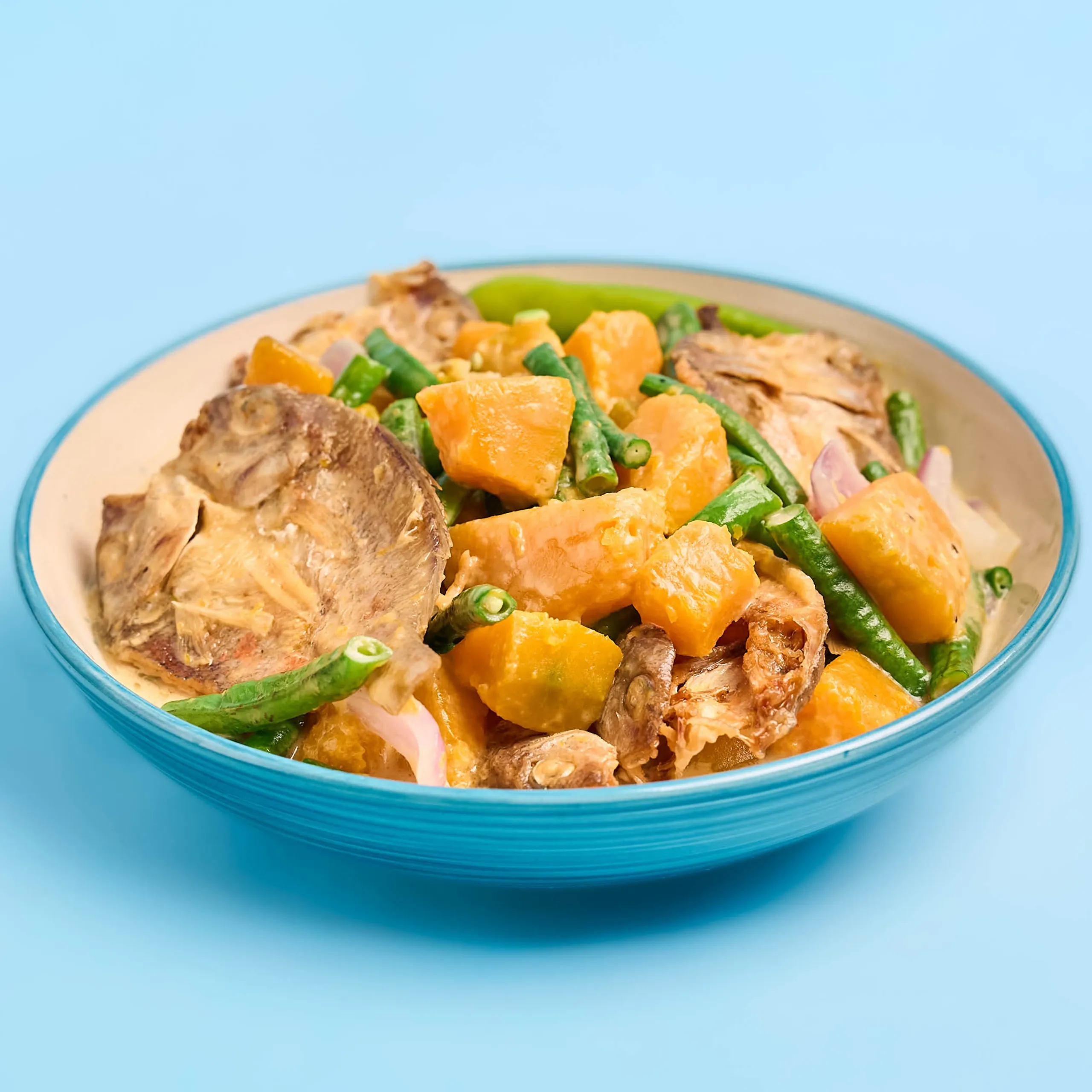 Close-up of a plate with cooked beef, diced carrots, green beans, and onions; a colorful mixed dish on a blue plate in focus.