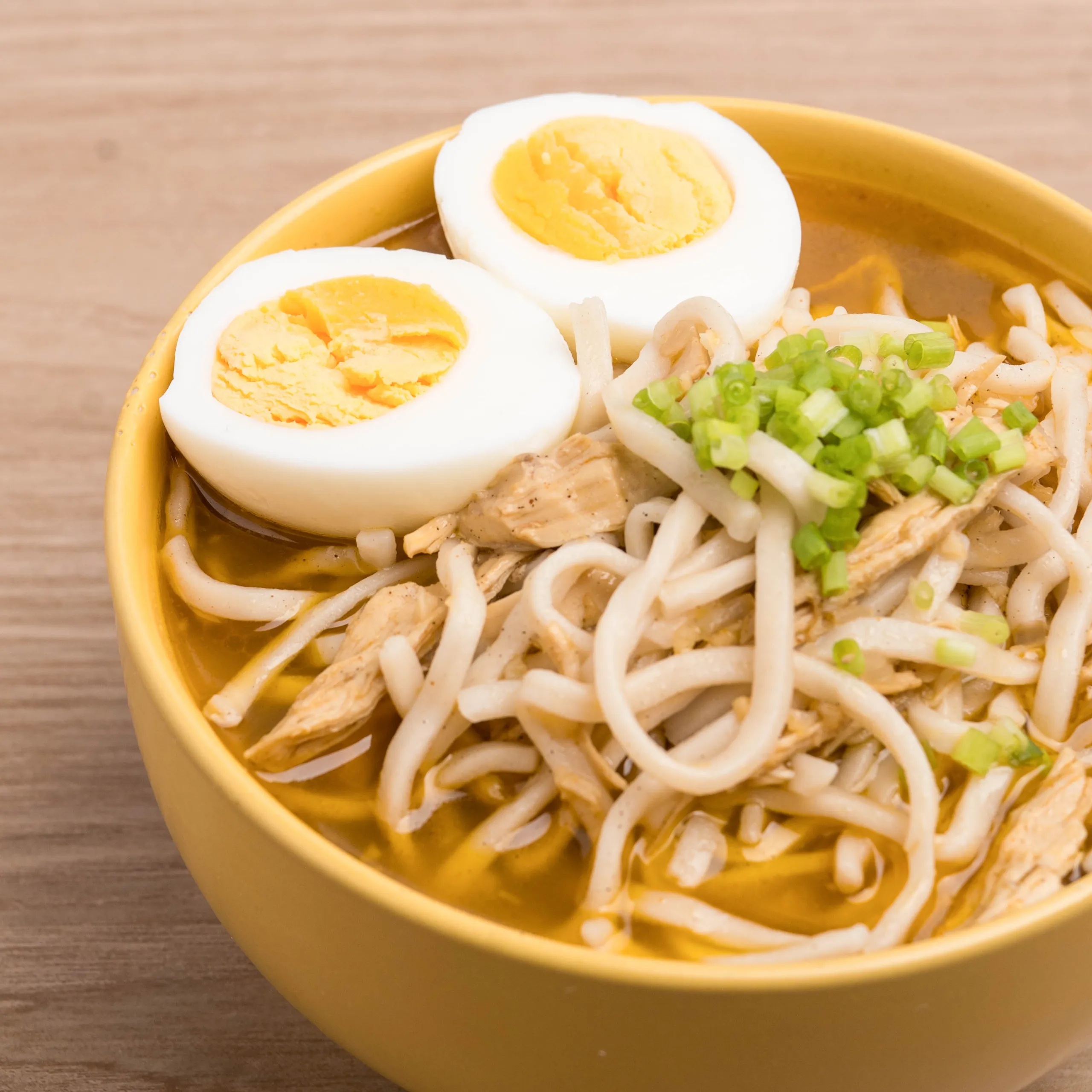 Two halves of hard-boiled egg resting on noodles with chopped green onions in a yellow bowl
