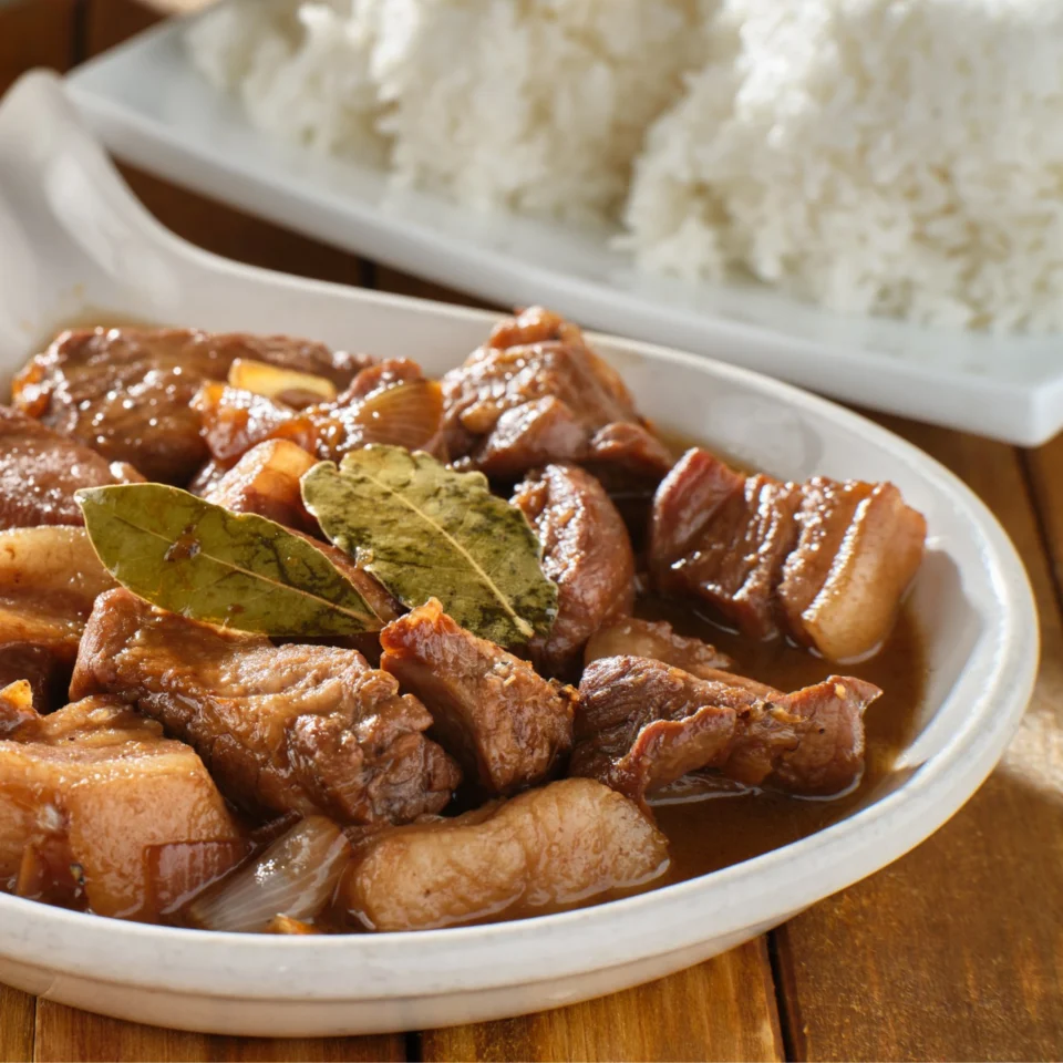 Pile of glazed braised beef chunks with bay leaves on a white plate on a wooden table