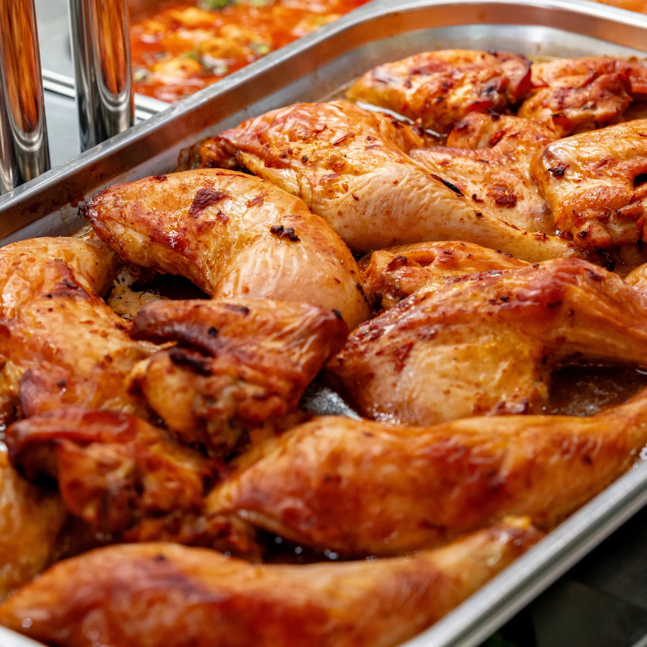 Tray of golden brown roasted chicken pieces with crispy skin in a metal pan, juices pooling around them