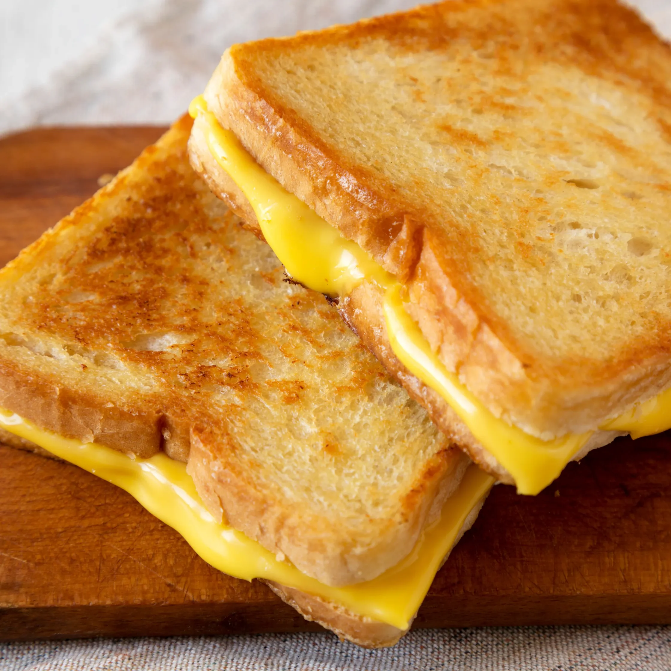 Close-up of a grilled cheese sandwich with melted cheddar between golden-brown bread on a wooden board.
