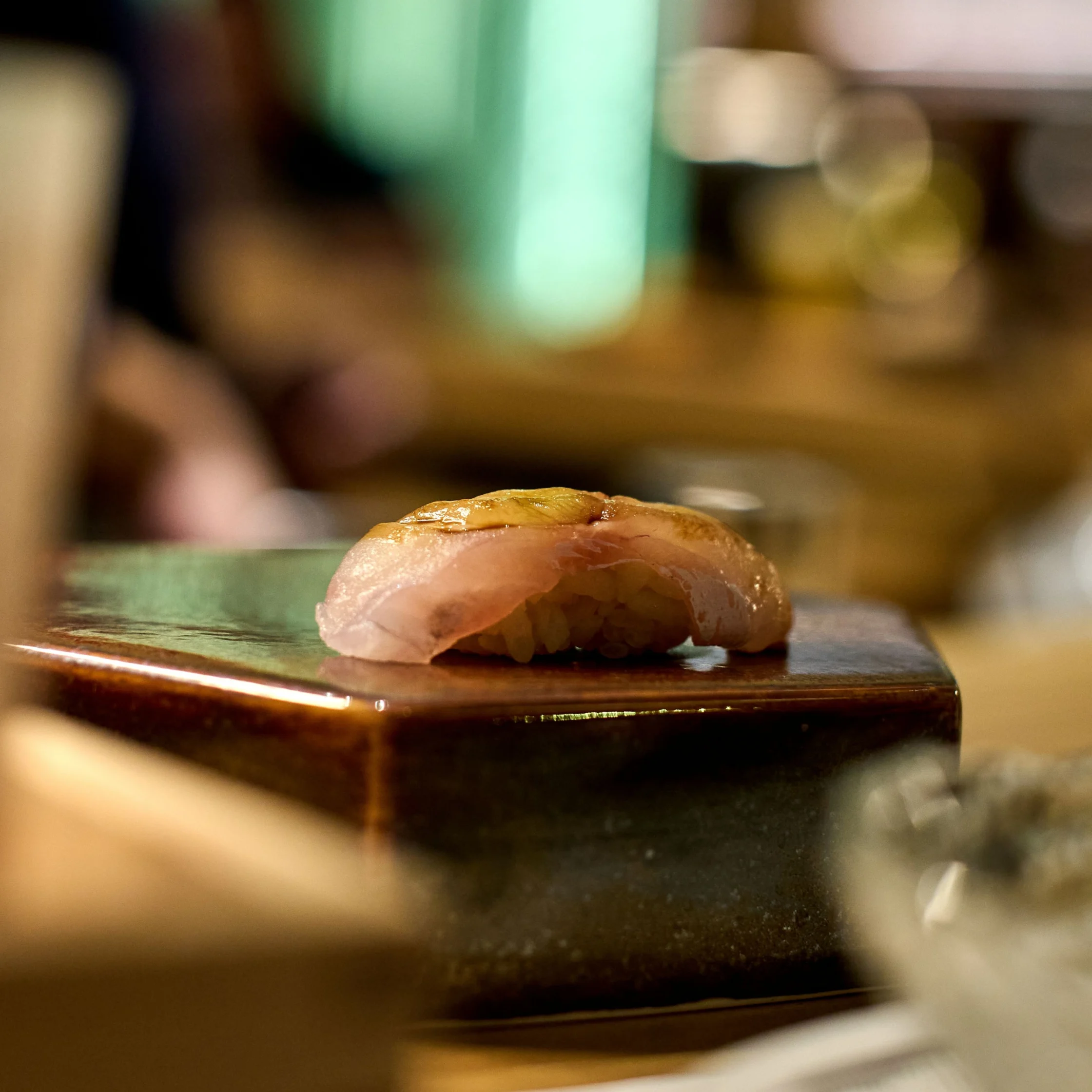 Close-up of a flaky pastry on a dark table, with a blurred kitchen background behind it.