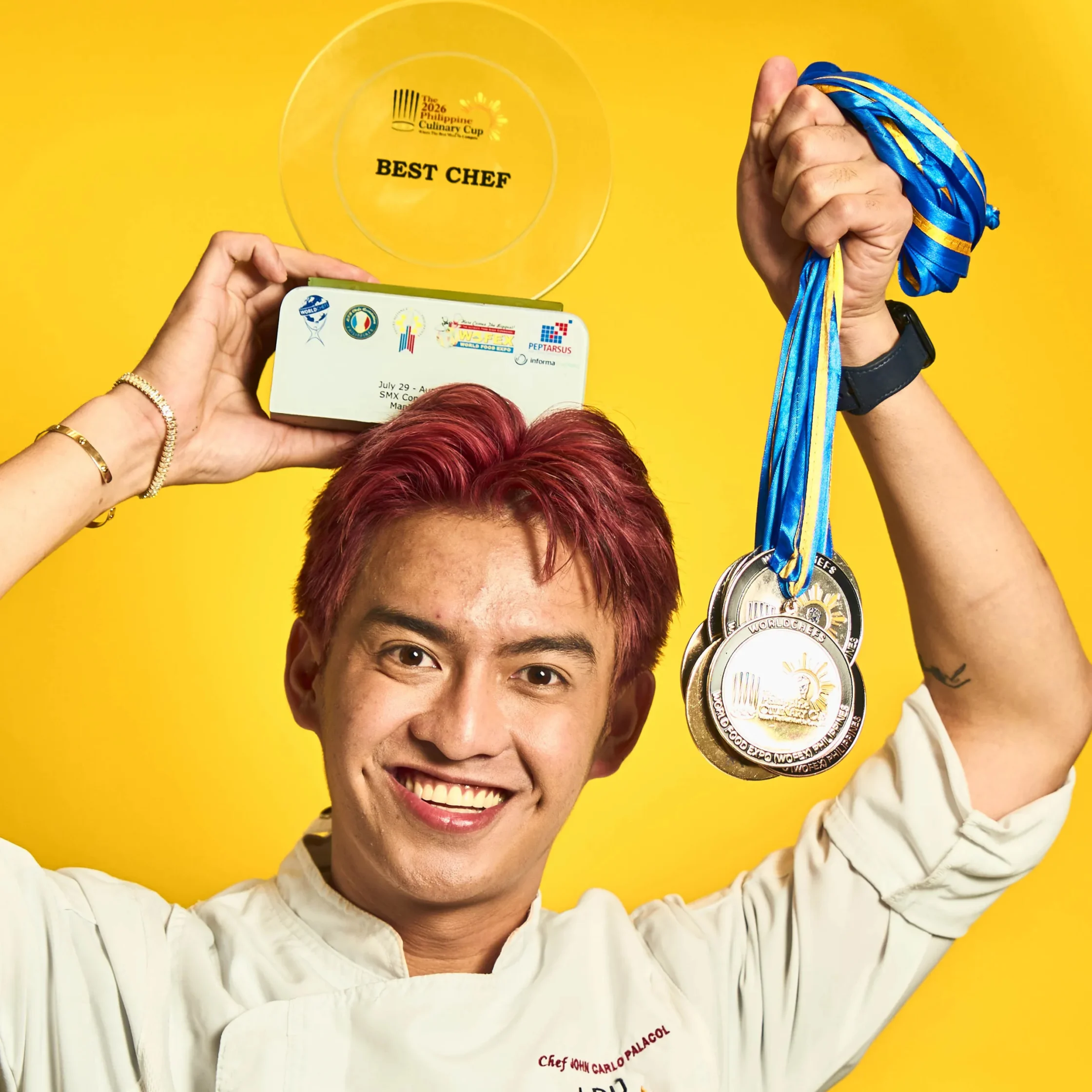 Celebrating a chef with multiple medals around the neck and a trophy that reads Best Chef against a bright yellow background Best Chef of the Year chef John Carlo Palacol