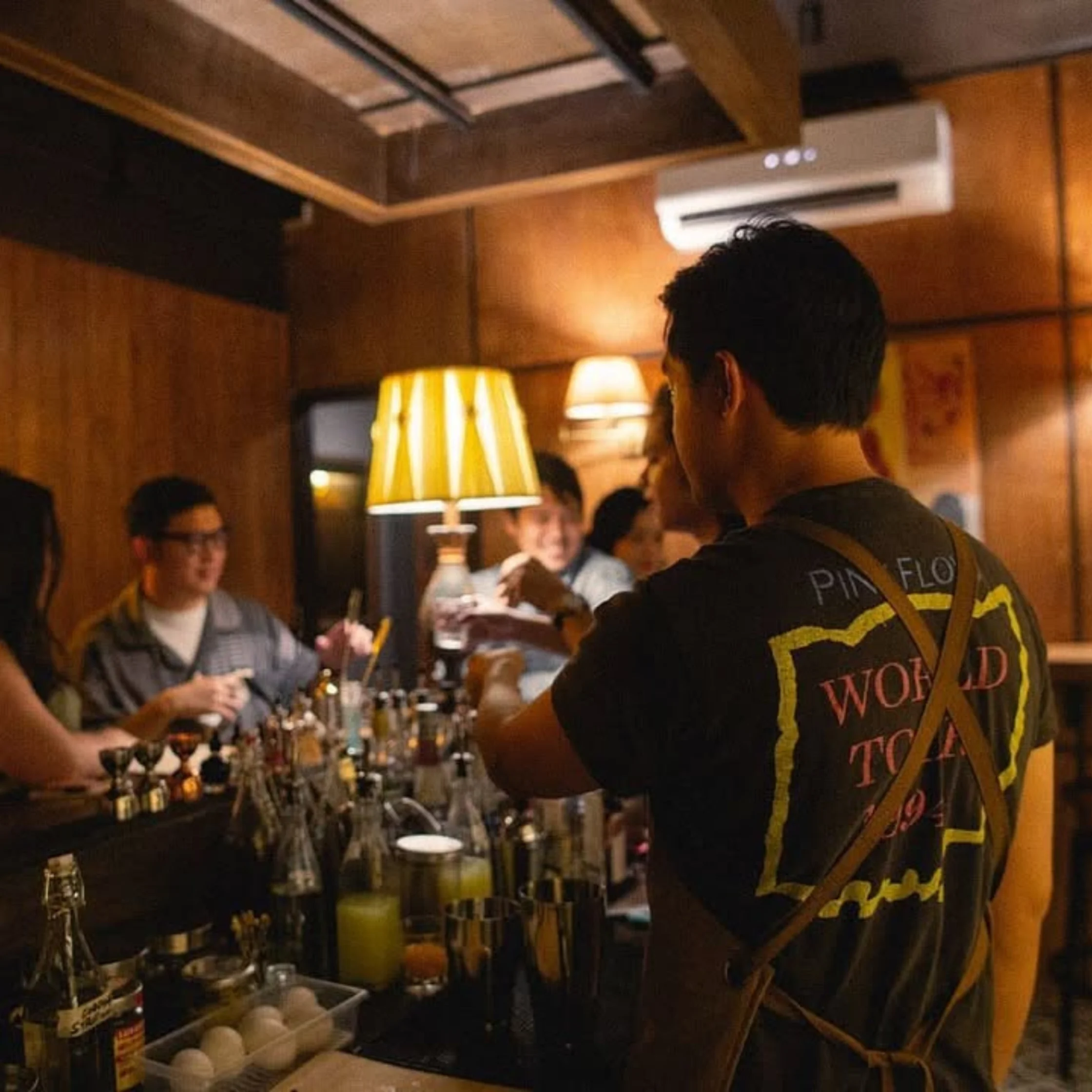 Back view of a person wearing a dark jacket with a large Pink Floyd patch in a crowded bar; bottles and bar setup visible in the background.