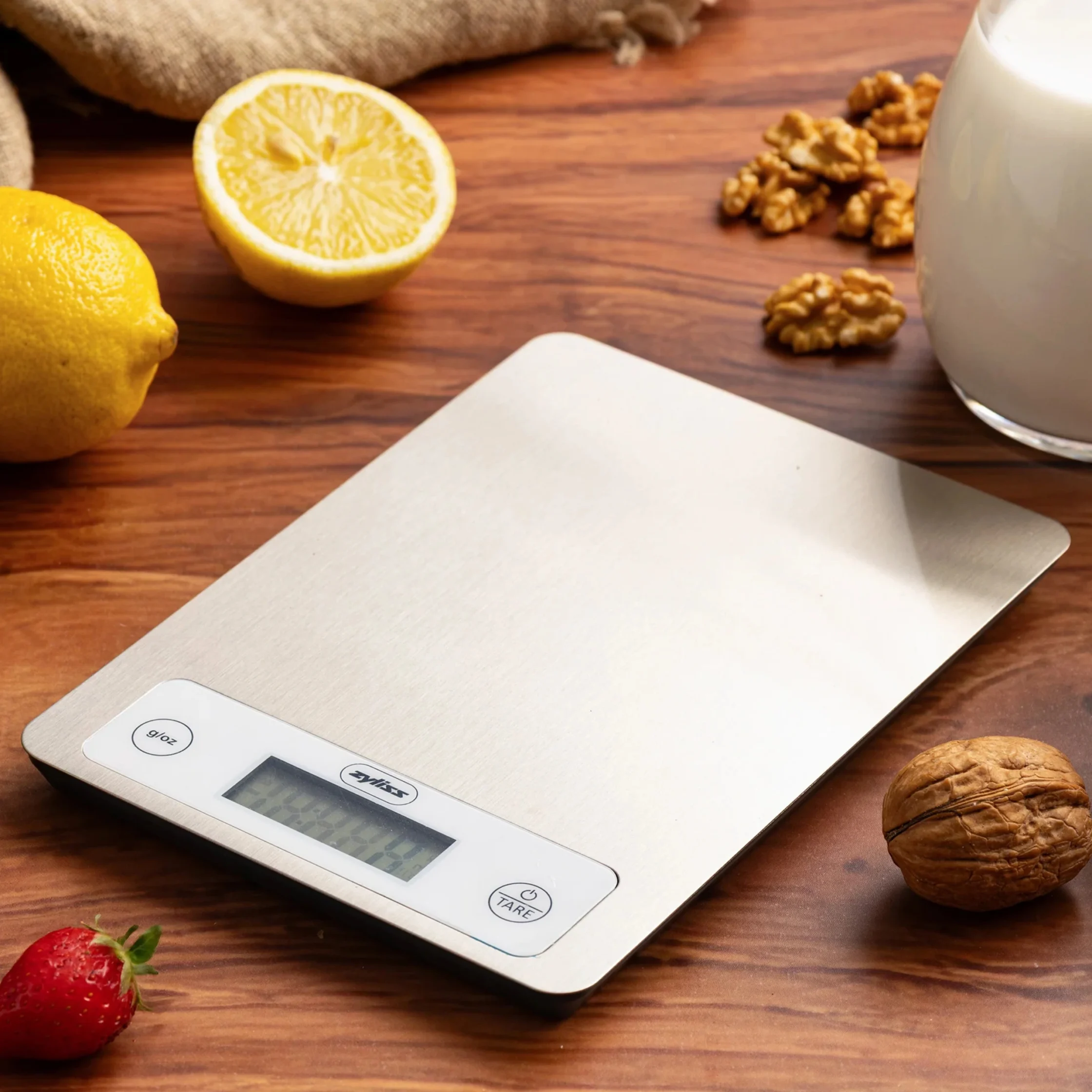 A digital kitchen scale on a wooden table beside lemons, walnuts, and a strawberry in the foreground.