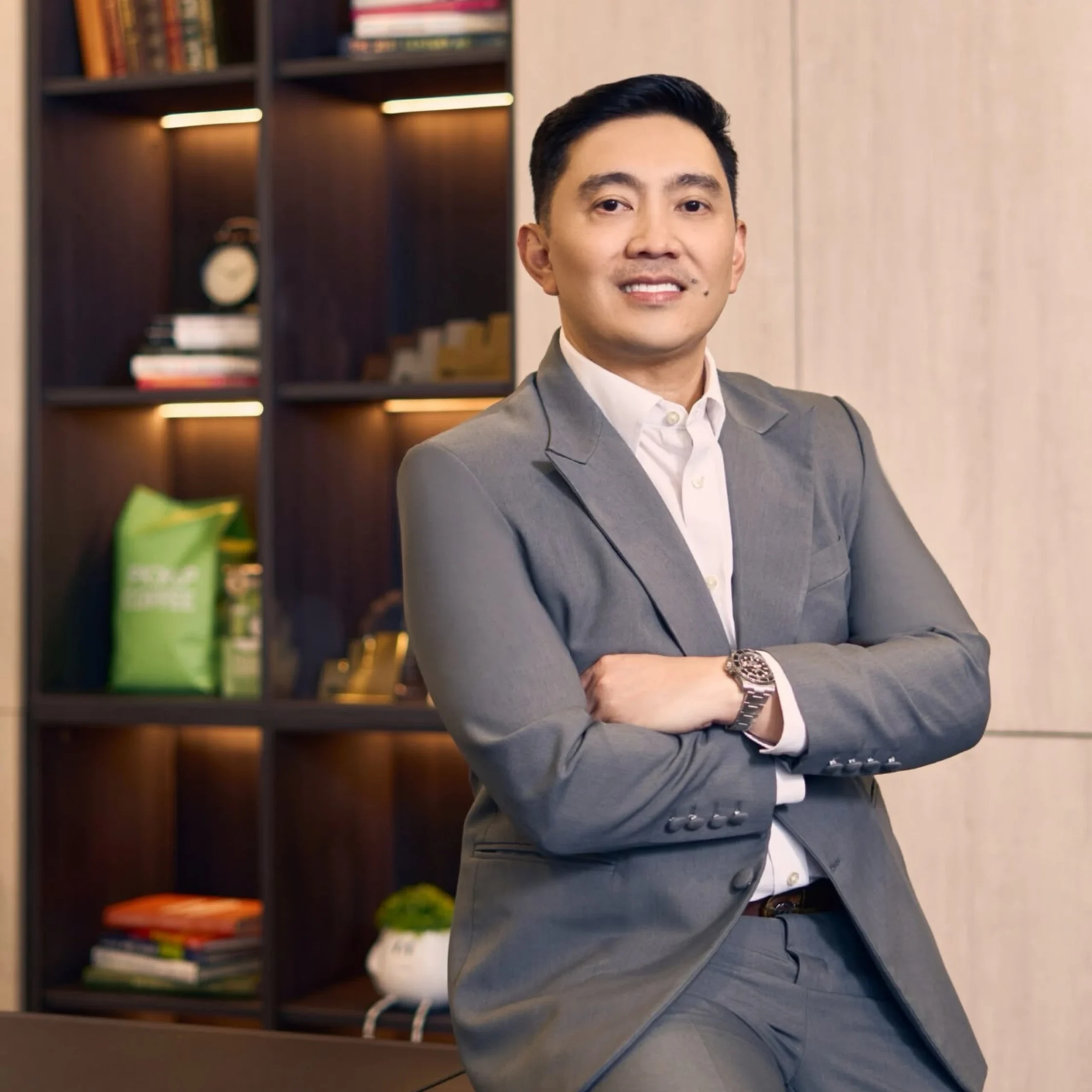 Professional man in a gray suit standing with arms crossed in an office setting.