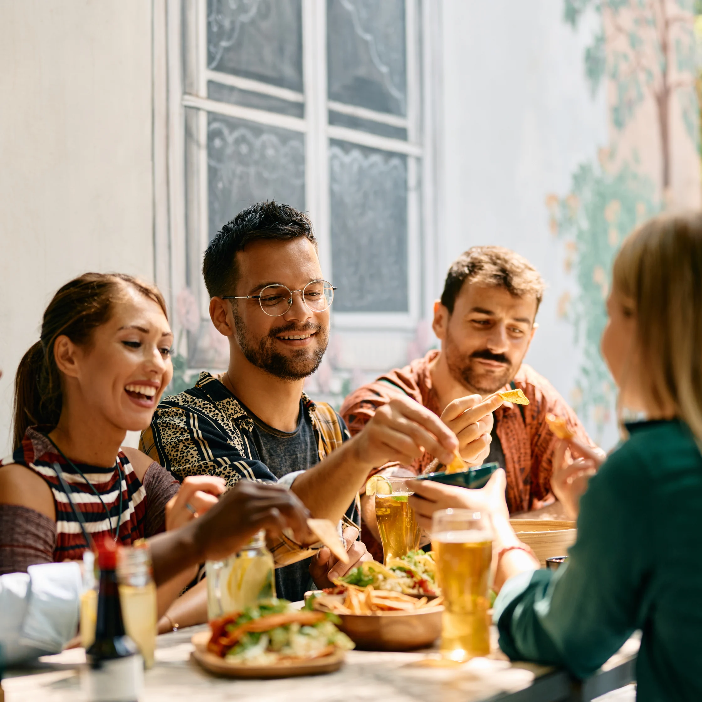 Group of friends at an outdoor table enjoying tacos and drinks, smiling and chatting.