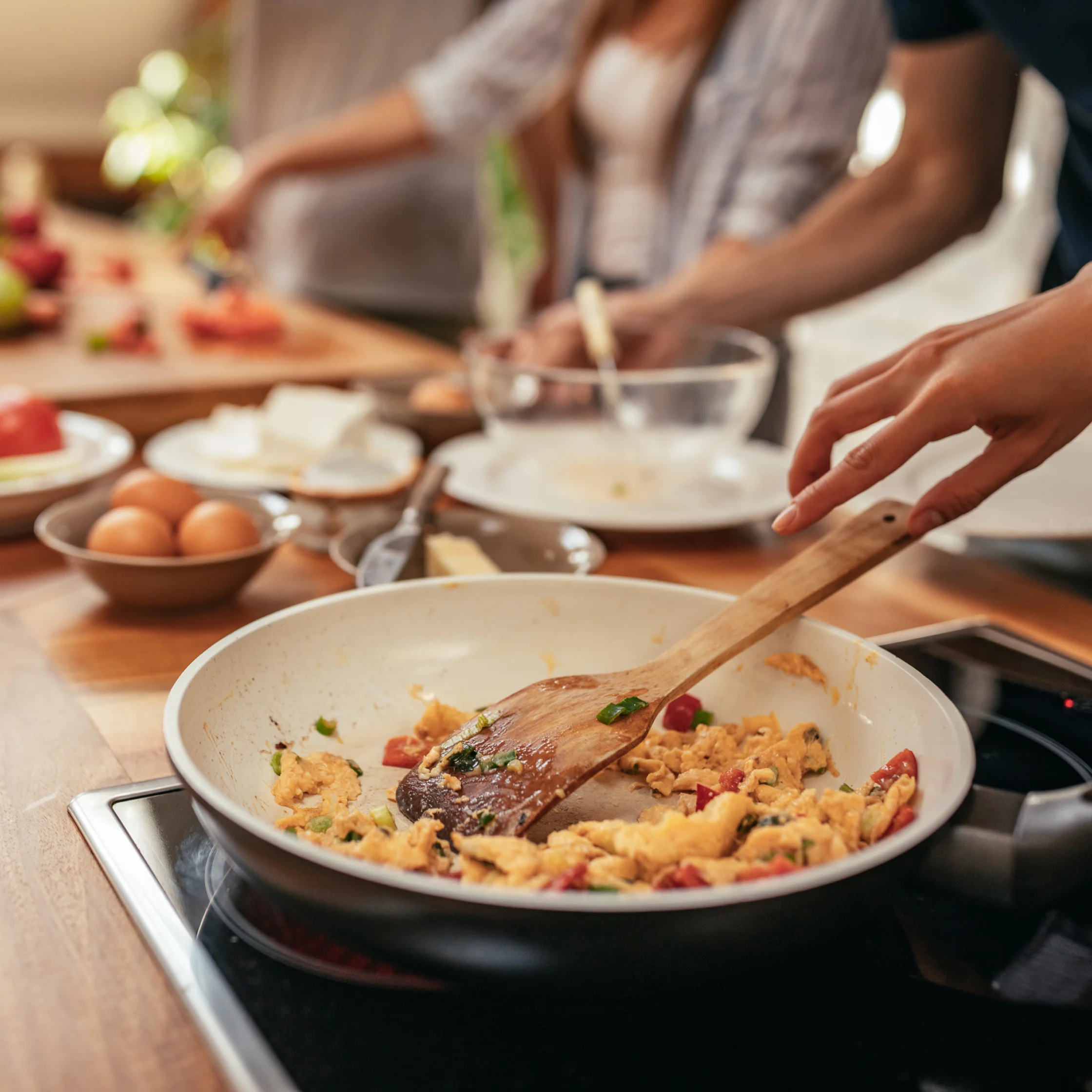 Hands stirring a vegetable scrambled egg dish in a white bowl on a stove.