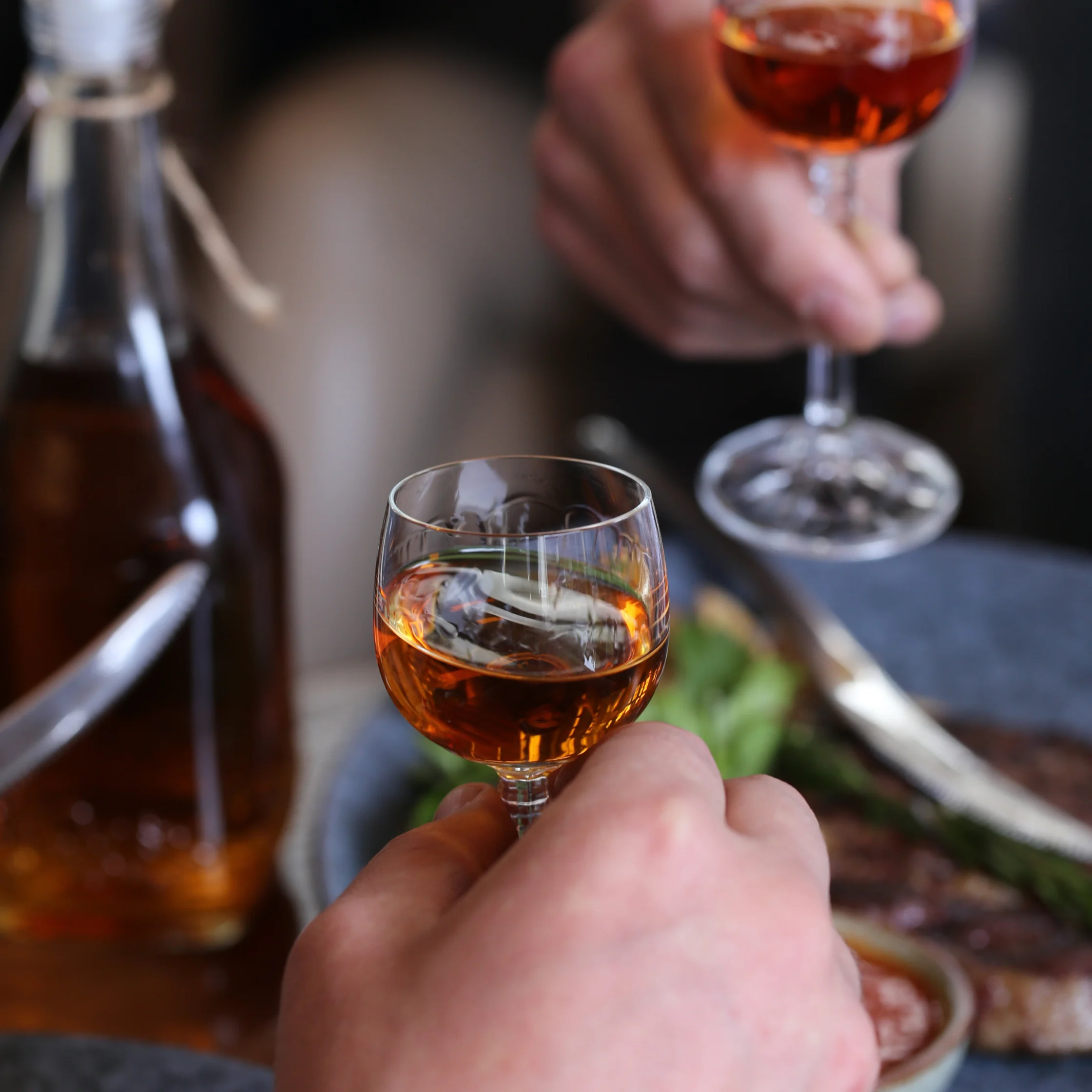 Close-up of hands toasting with amber-colored wine glasses.