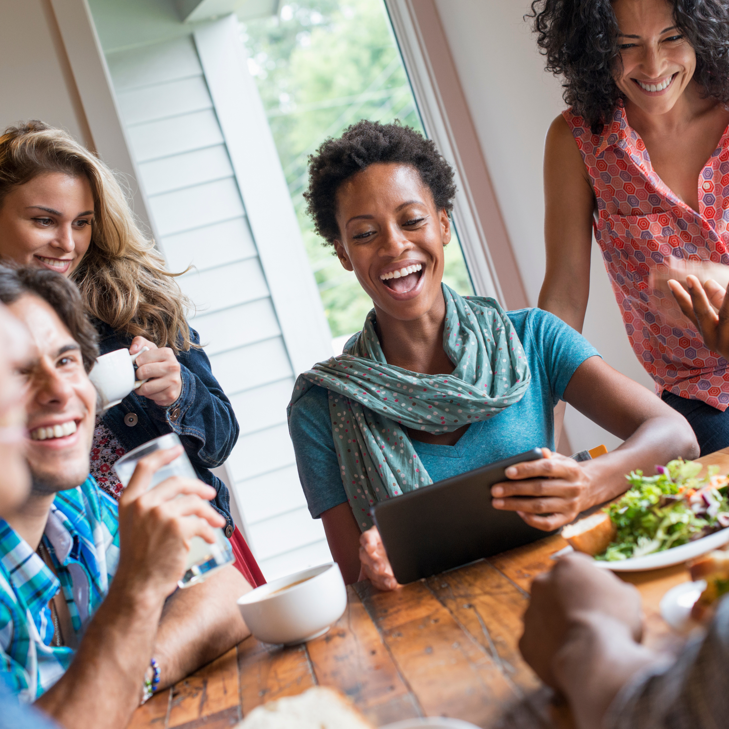 Group of friends around a wooden table sharing a meal, laughing together.
