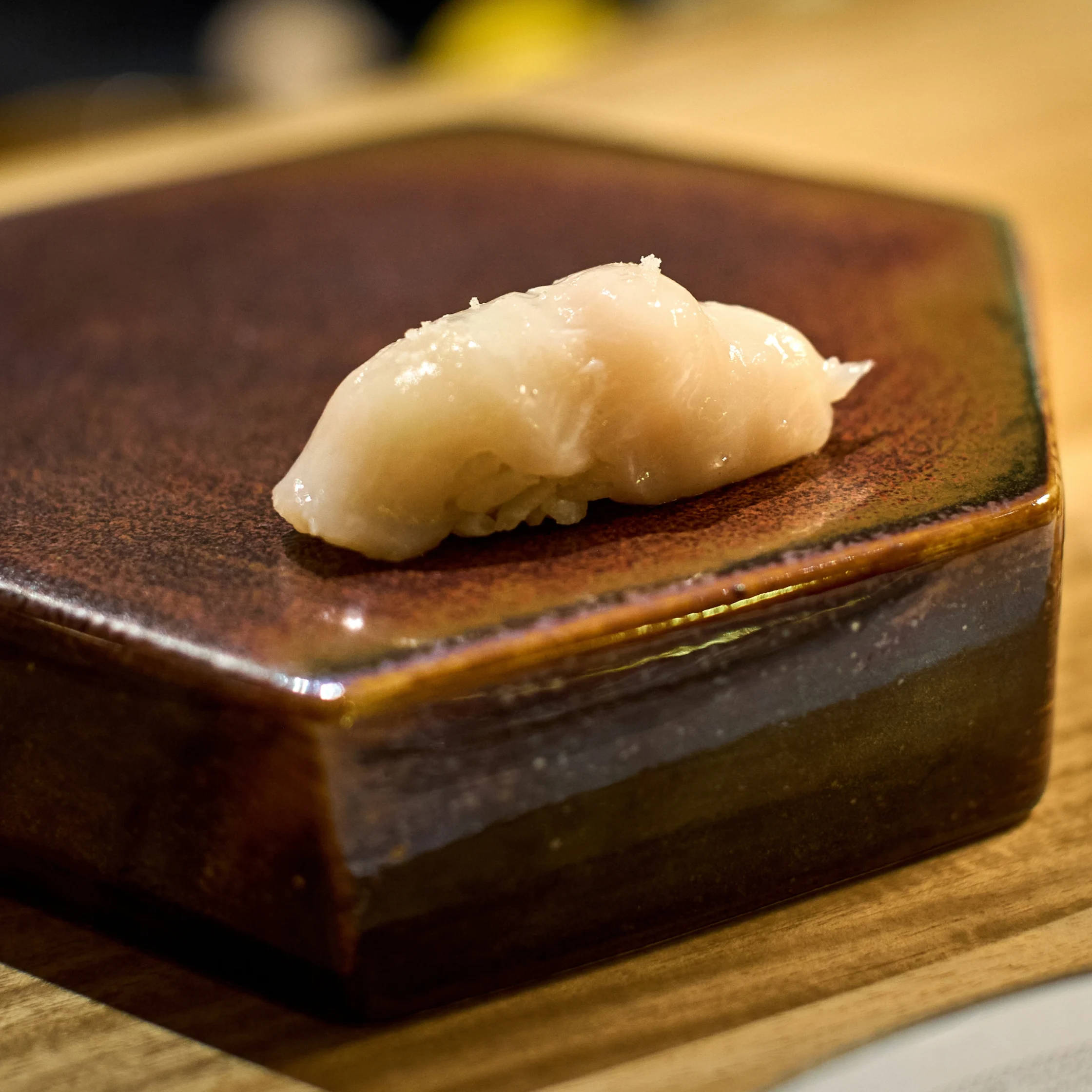 Close-up of a single white fish nigiri sushi on a brown ceramic plate, focus on the glossy slice over rice.