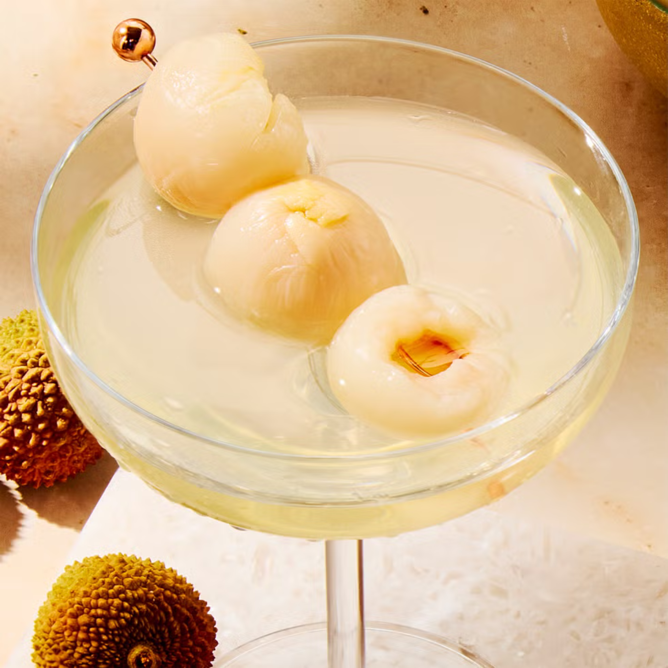 Close-up of a glass with a pale milk-like liquid and peeled lychee fruits resting in and around the rim on a light wooden surface.