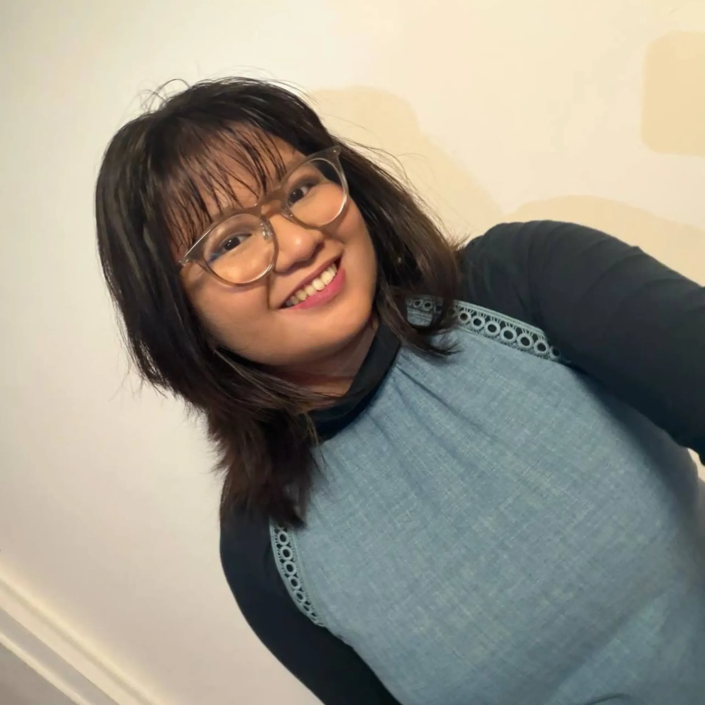 Smiling woman with glasses tilted at an angle, wearing a blue top, against a light background.