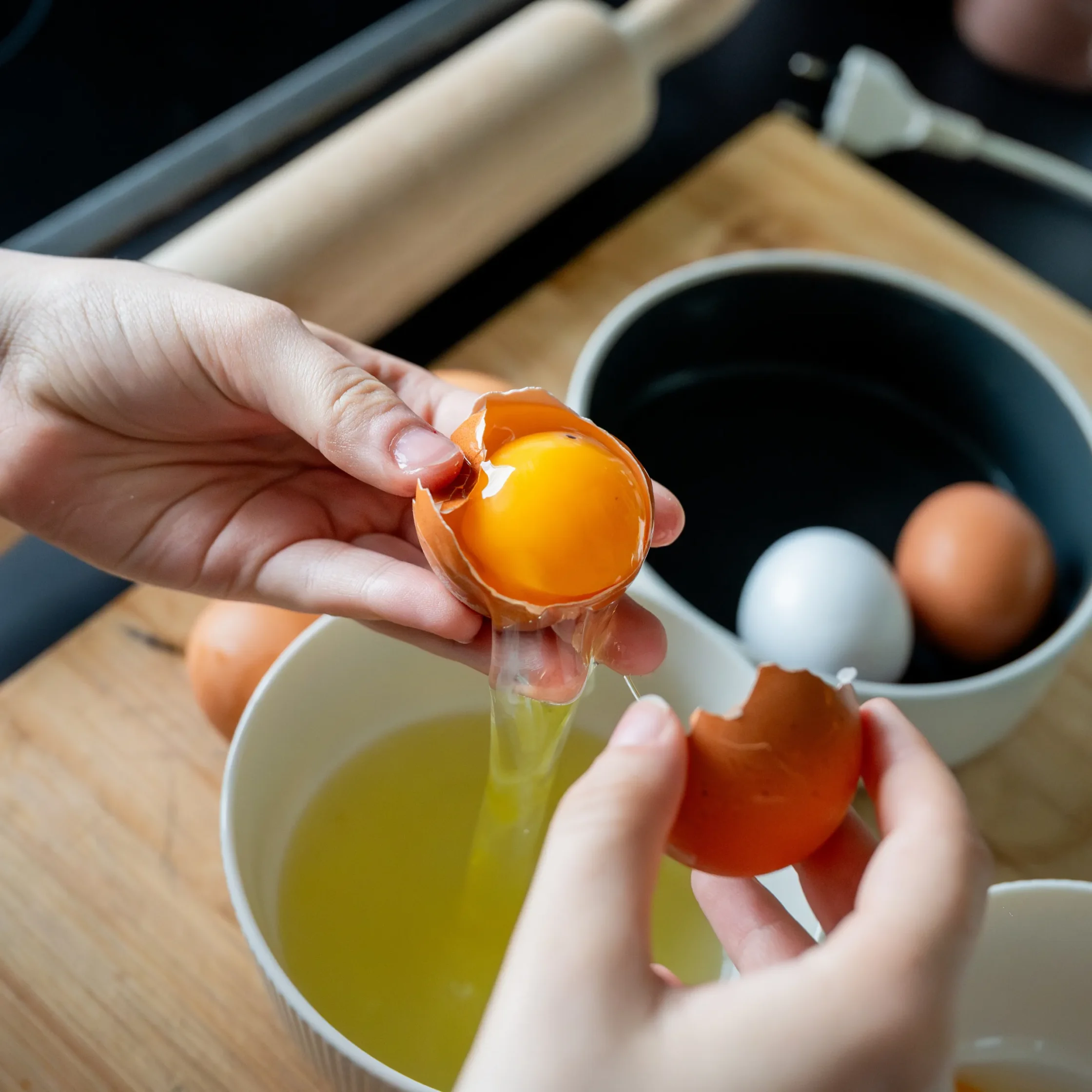 Person cracking an orange egg over a bowl, peeling shell with fingers visible in the foreground.