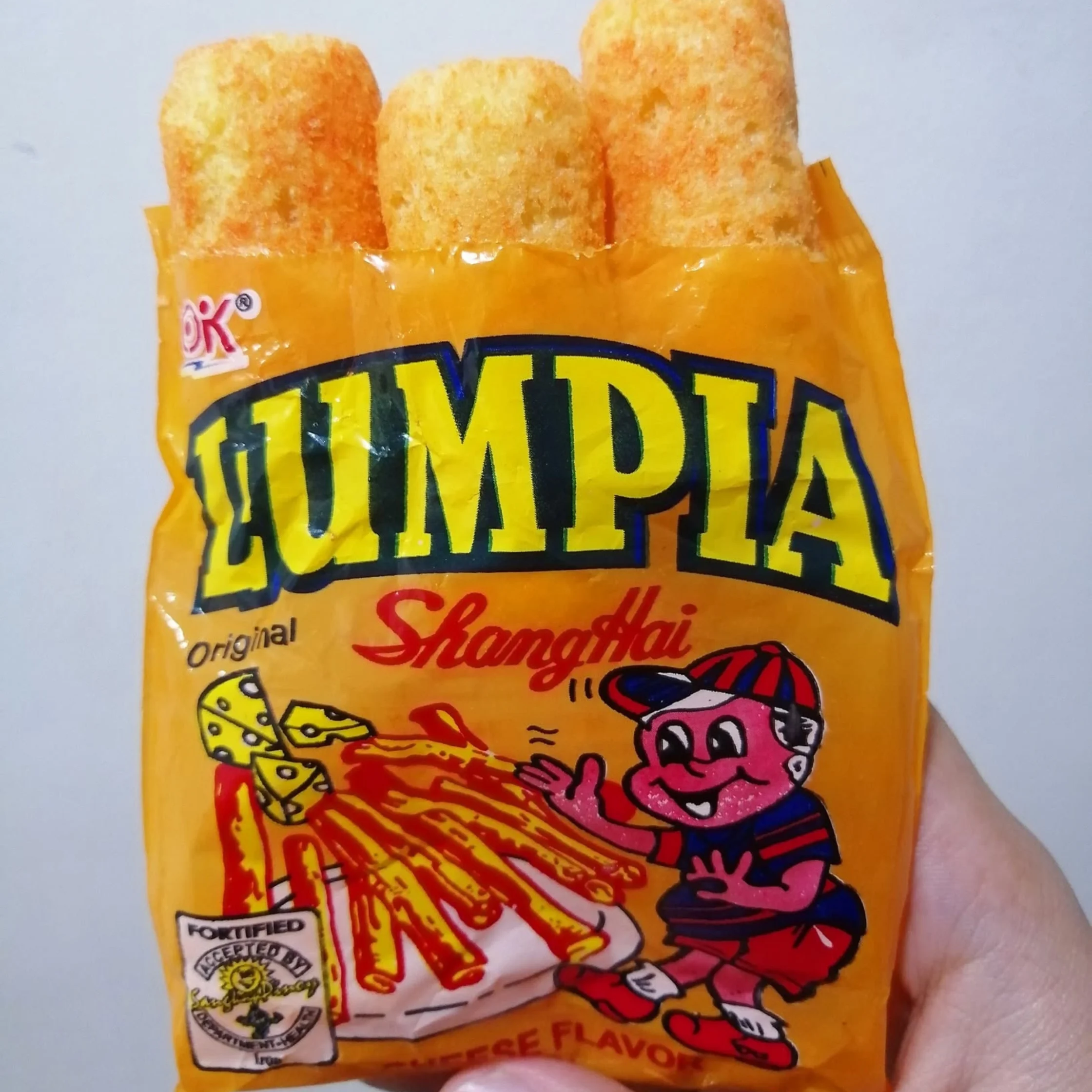 Orange bag of cheese-flavored snacks with three puffed pieces visible at the top, plus colorful cartoon graphics on the packaging.Lumpia Shanghai PHOTO COURTESY OF The Fat Gourmand Official Facebook