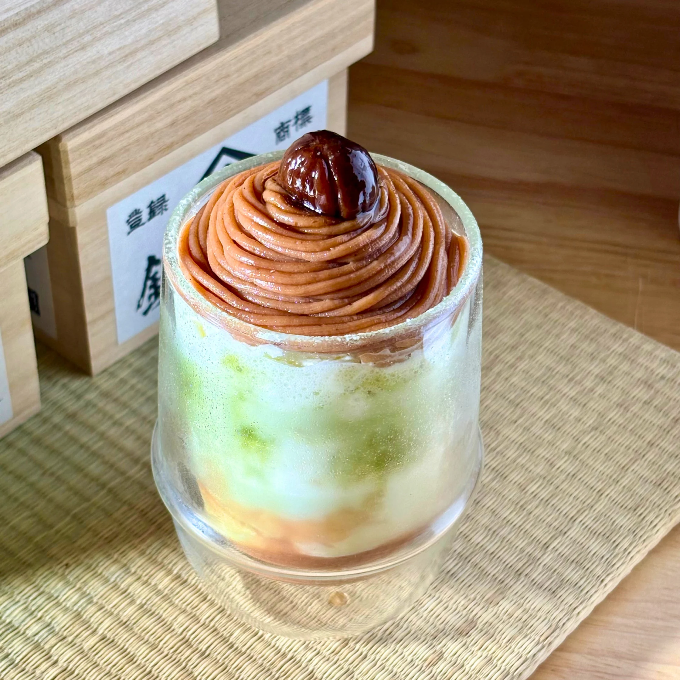Dessert cup with orange swirled frosting and a glossy chestnut on top, set in a clear cup on a woven placemat.