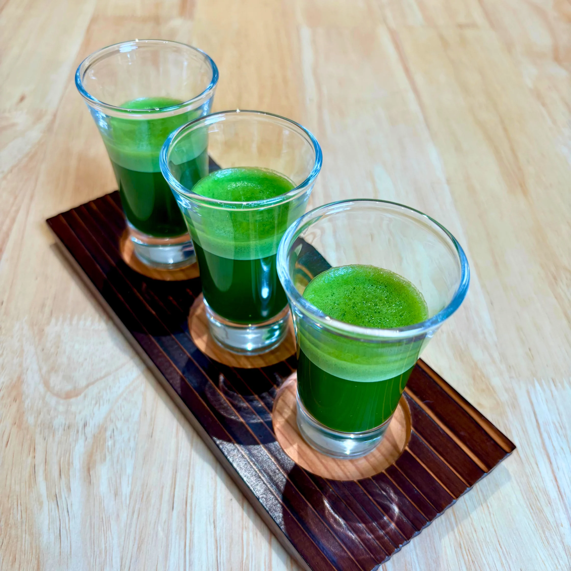 three small shot glasses filled with matcha on a dark wooden slab placed on a light wooden table