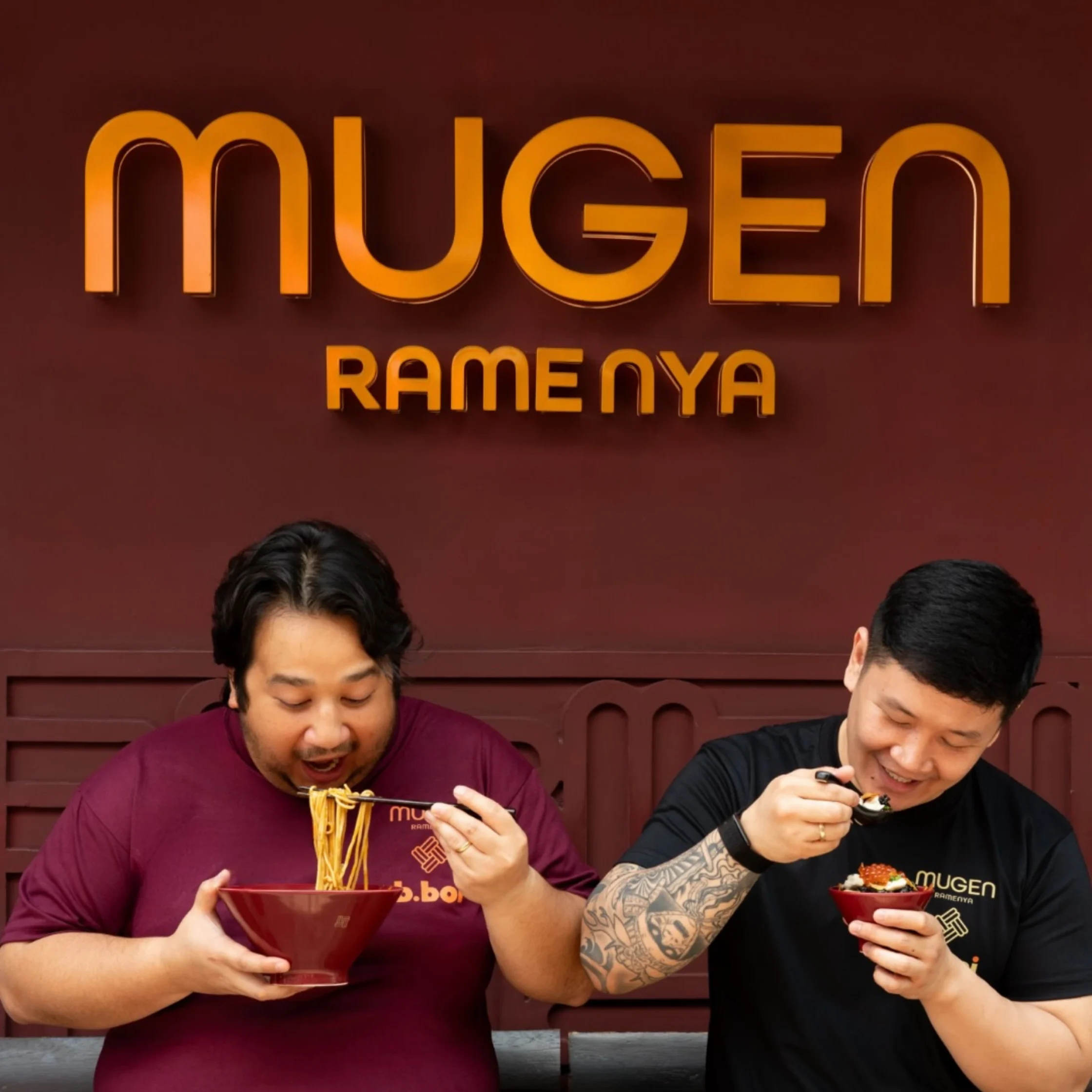 Two men eating ramen and sushi bowls at a ramen shop, with an orange sign reading Mugen Ramenya behind them.