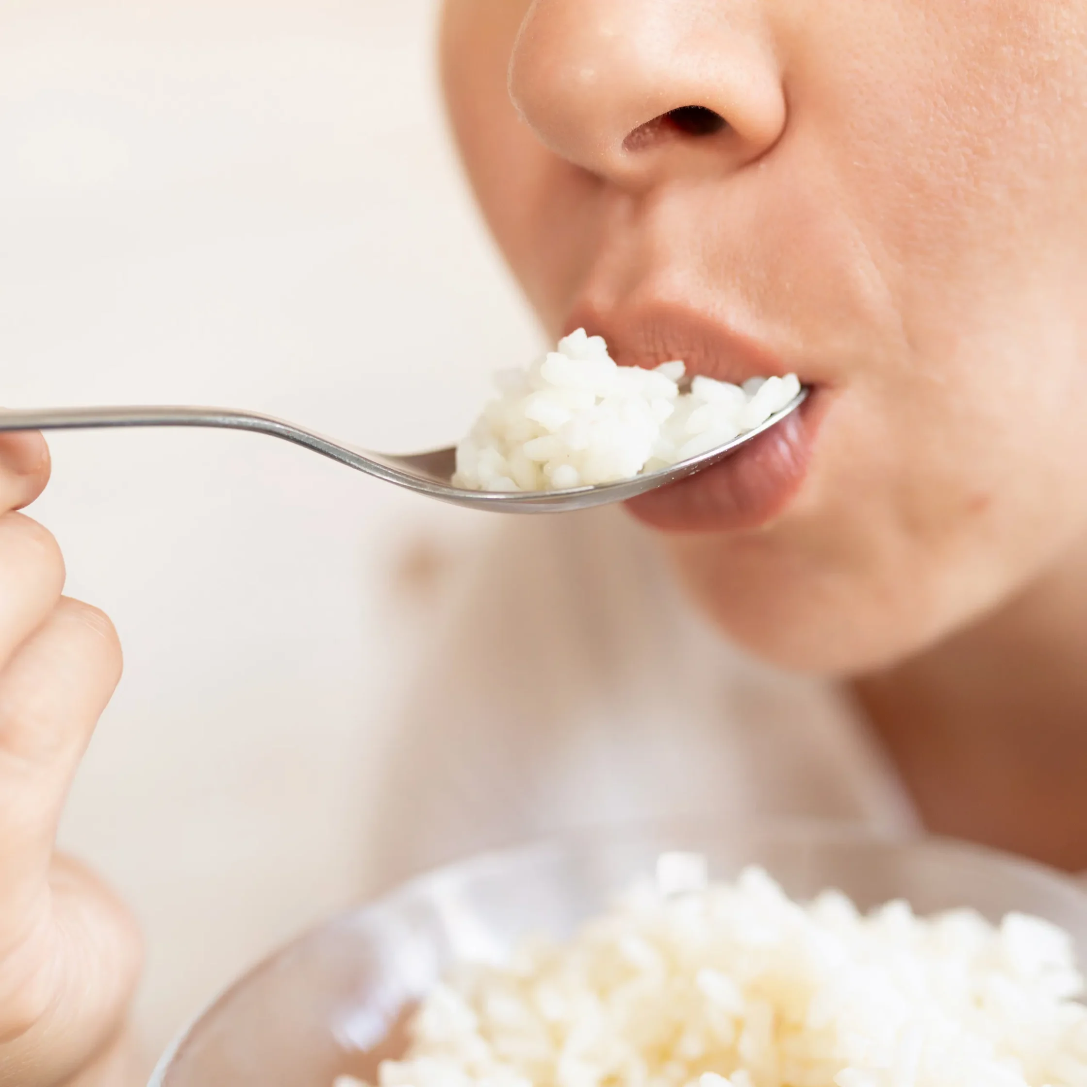 Close-up of a person bringing a spoonful of white rice toward their mouth for a bite.