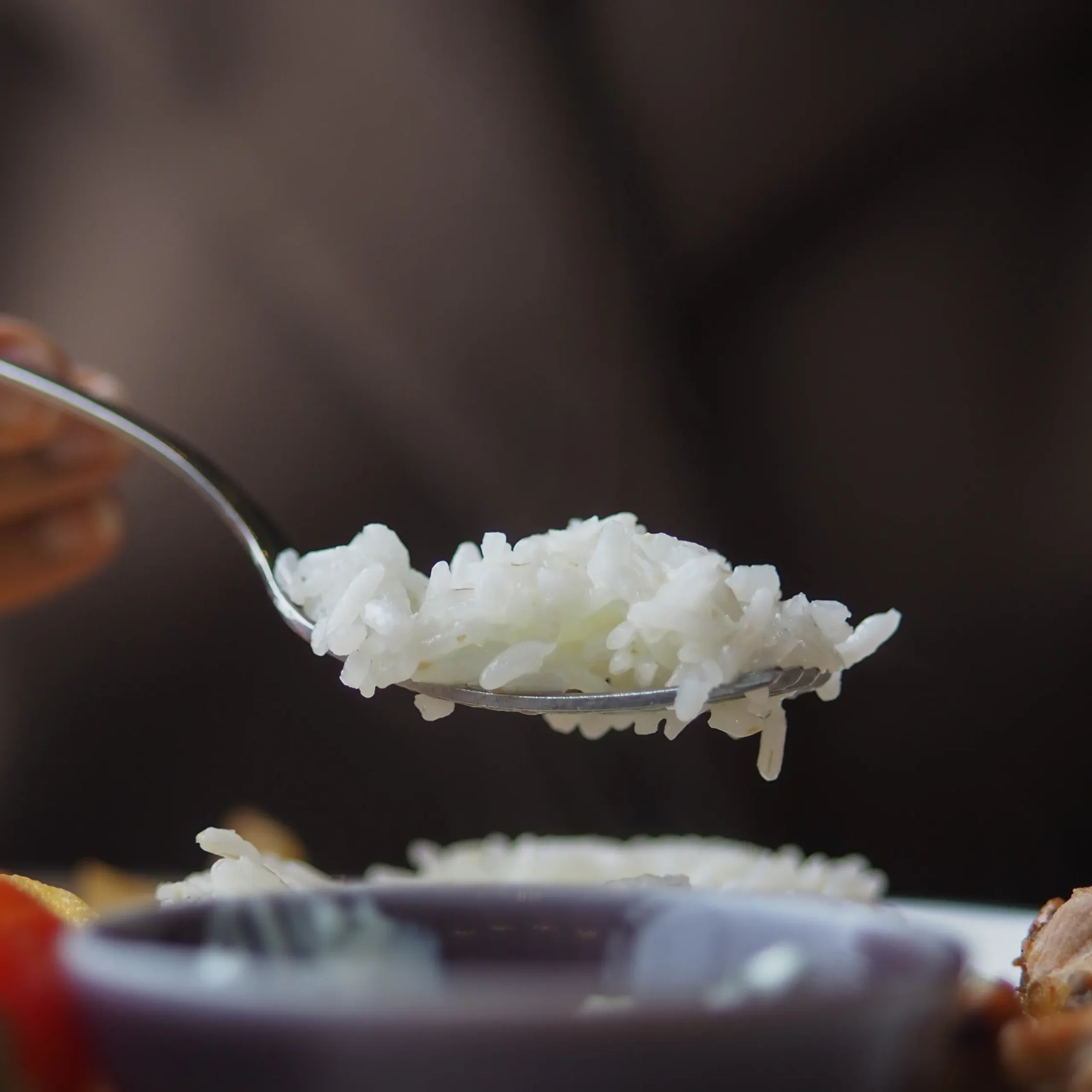 Close-up of white rice on a spoon against a dark, blurred background.