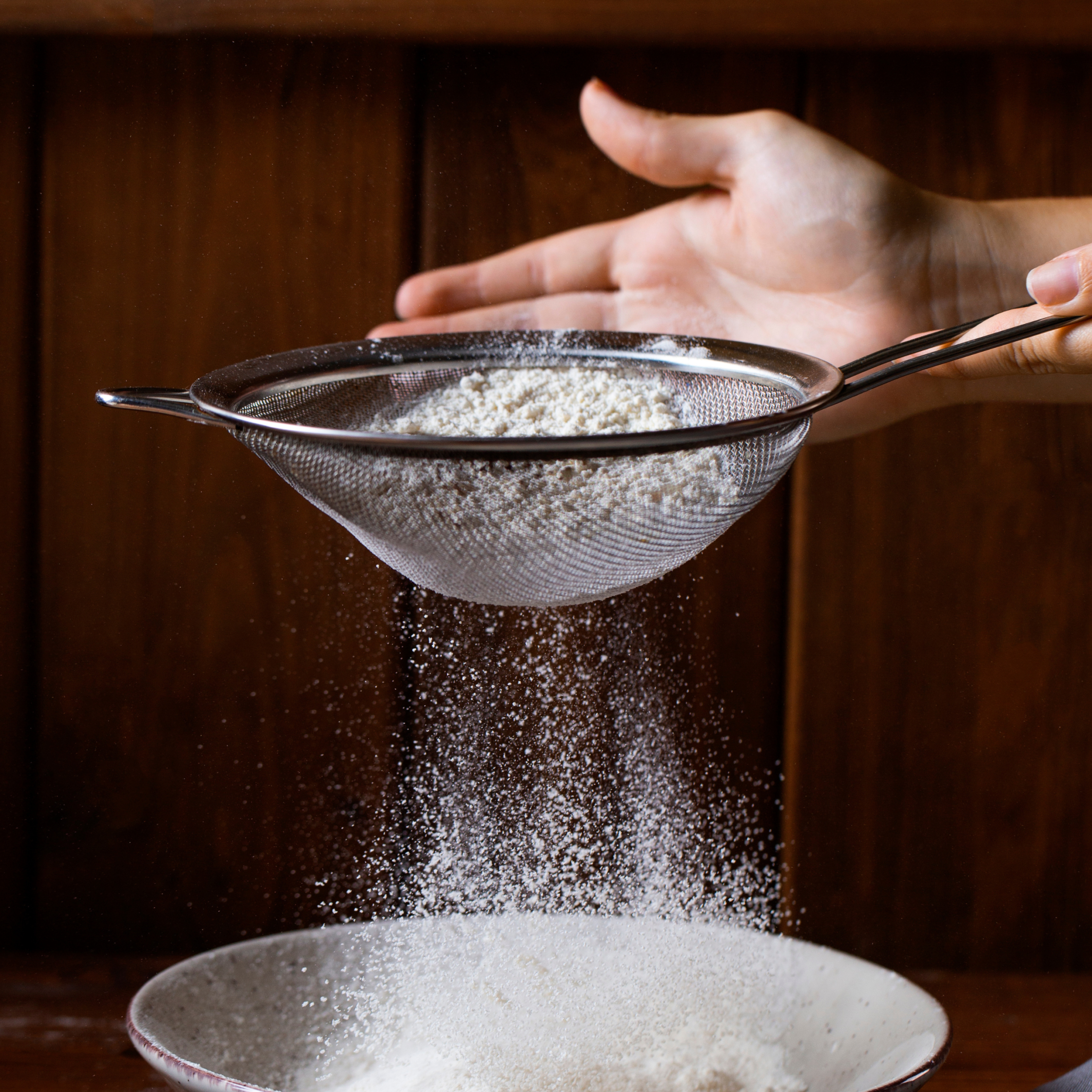 Hand tapping sieve with white powder falling into a bowl