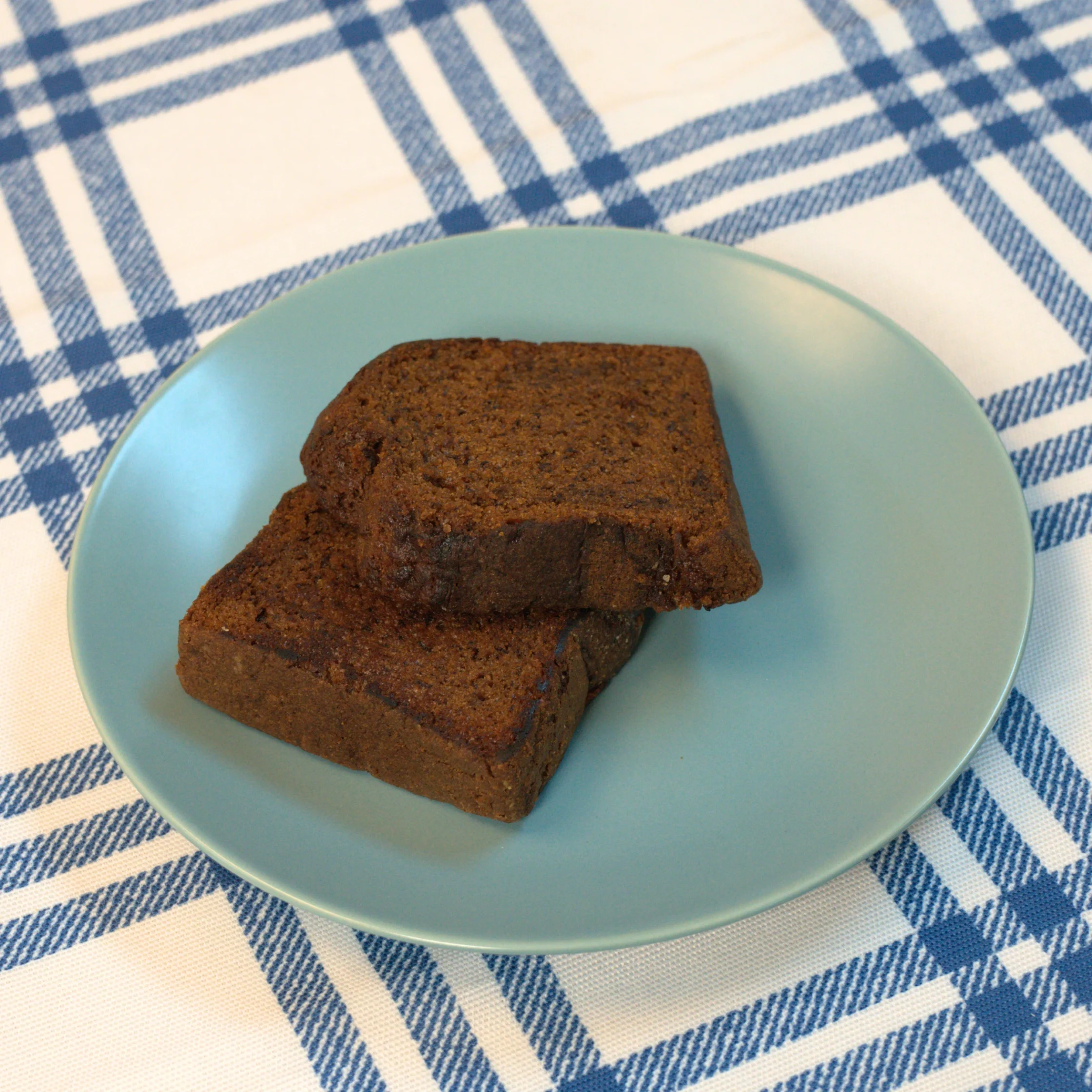 two dark slices of banana bread placed on a blue plate on a checkered table cloth