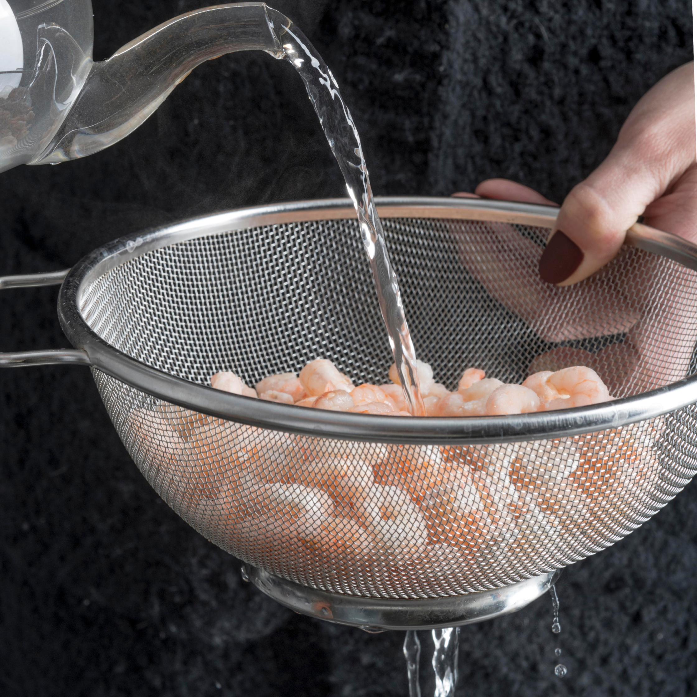 Water poured over shrimp inside a strainer