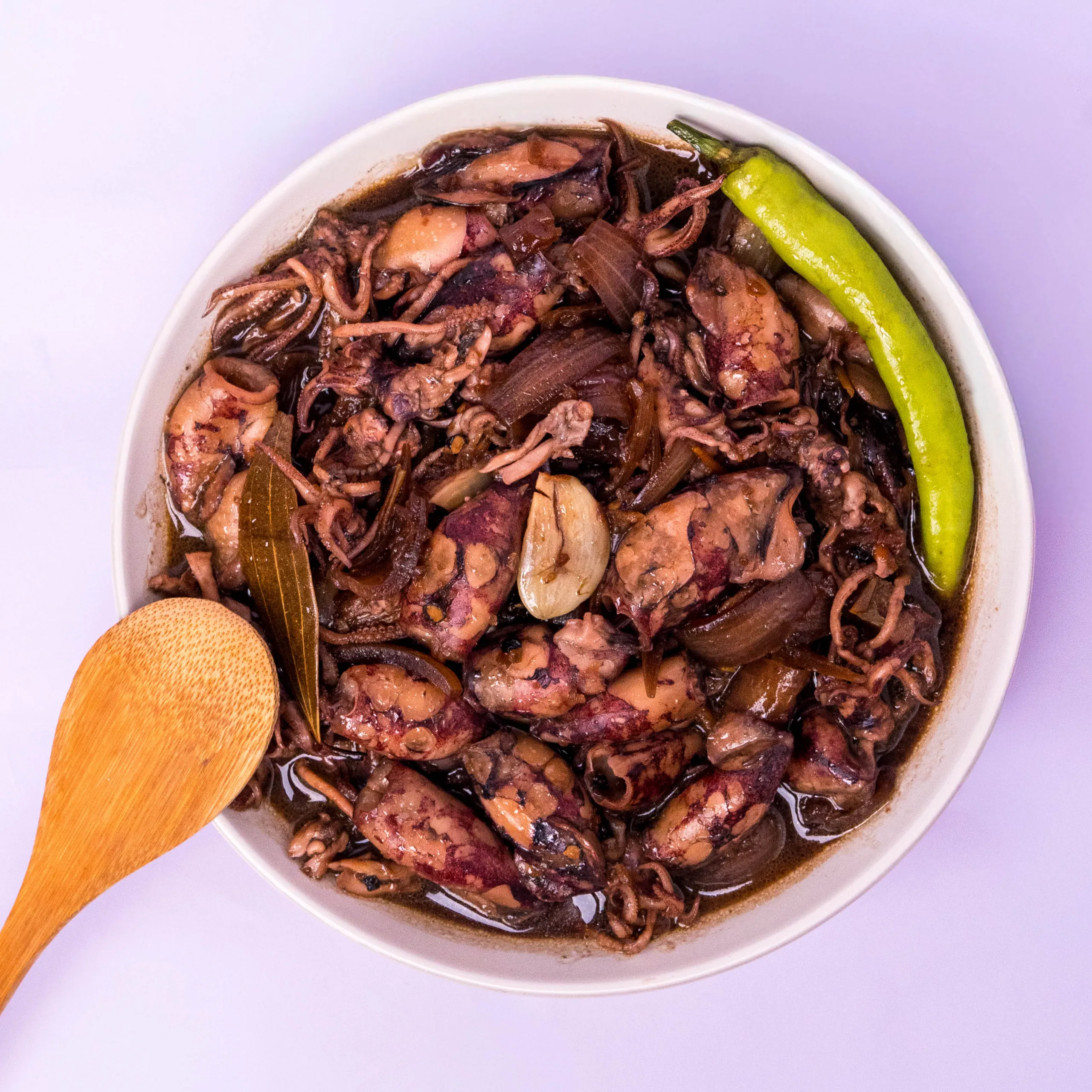 Top-down view of a white bowl of shredded beef stew with a green pepper and wooden spoon.