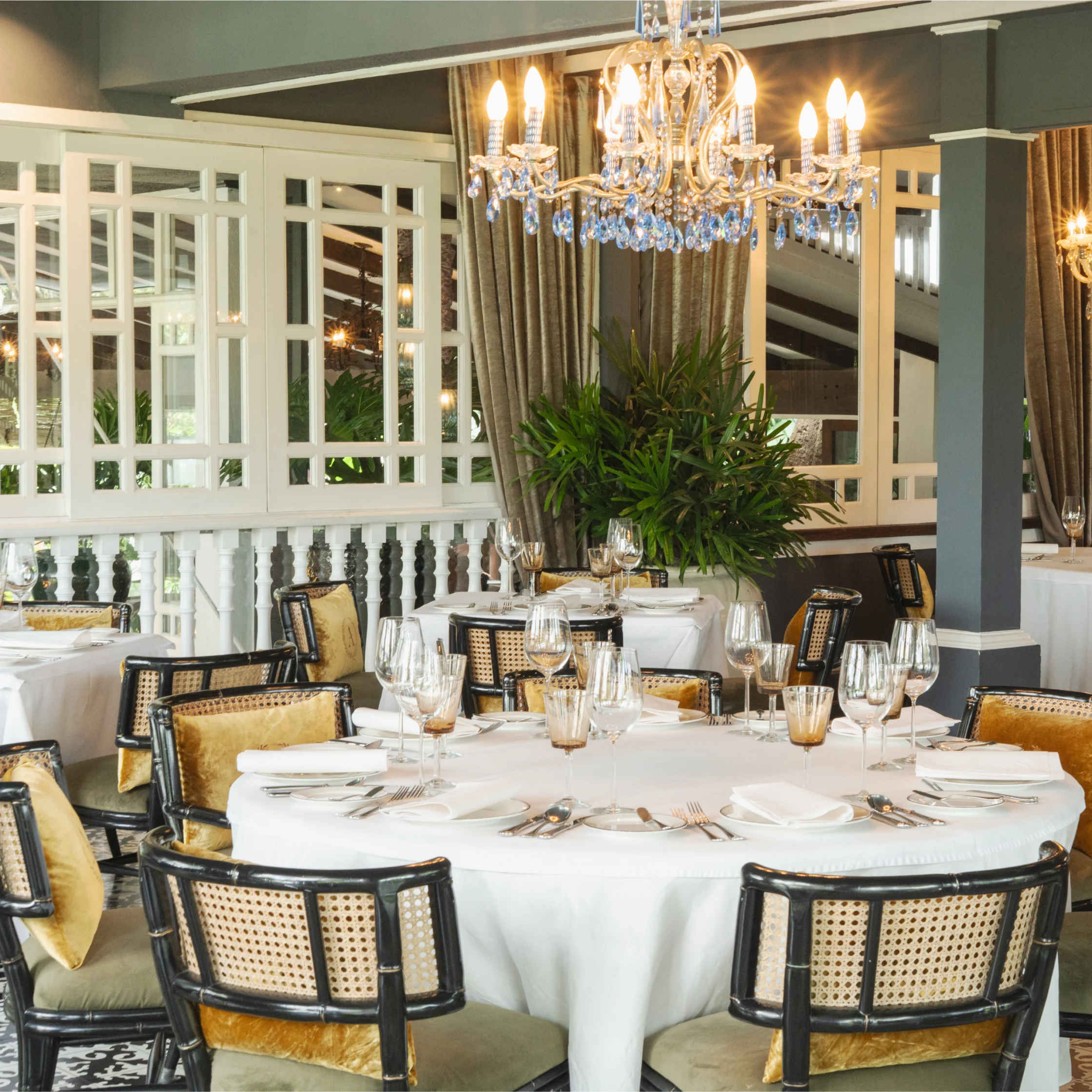 Elegant dining room with round tables, white tablecloths, glassware, and wicker chairs beneath crystal chandeliers basti escalante of antonio group_chefs room