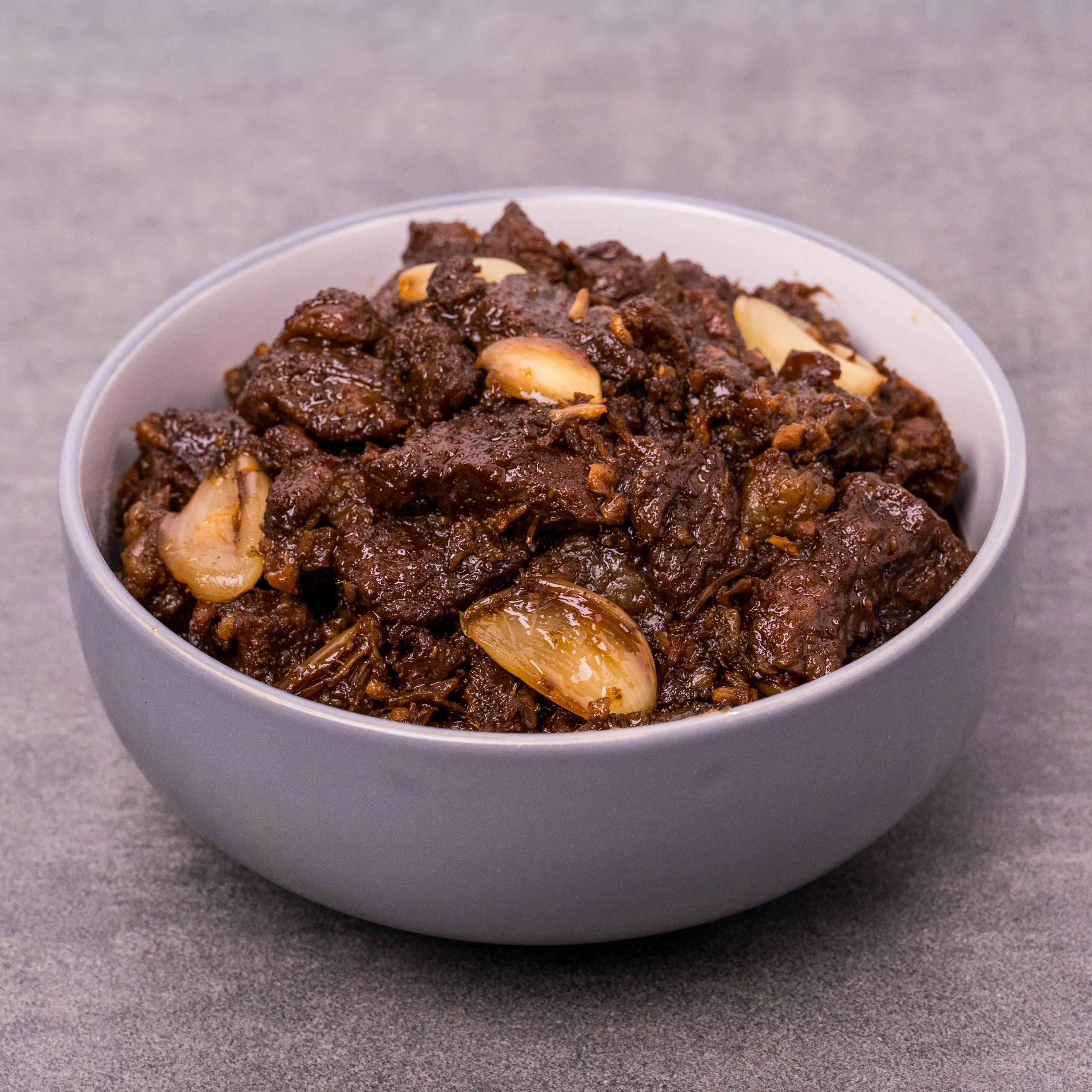 Close-up of a bowl of dark beef stew with chunky meat and onion pieces.
