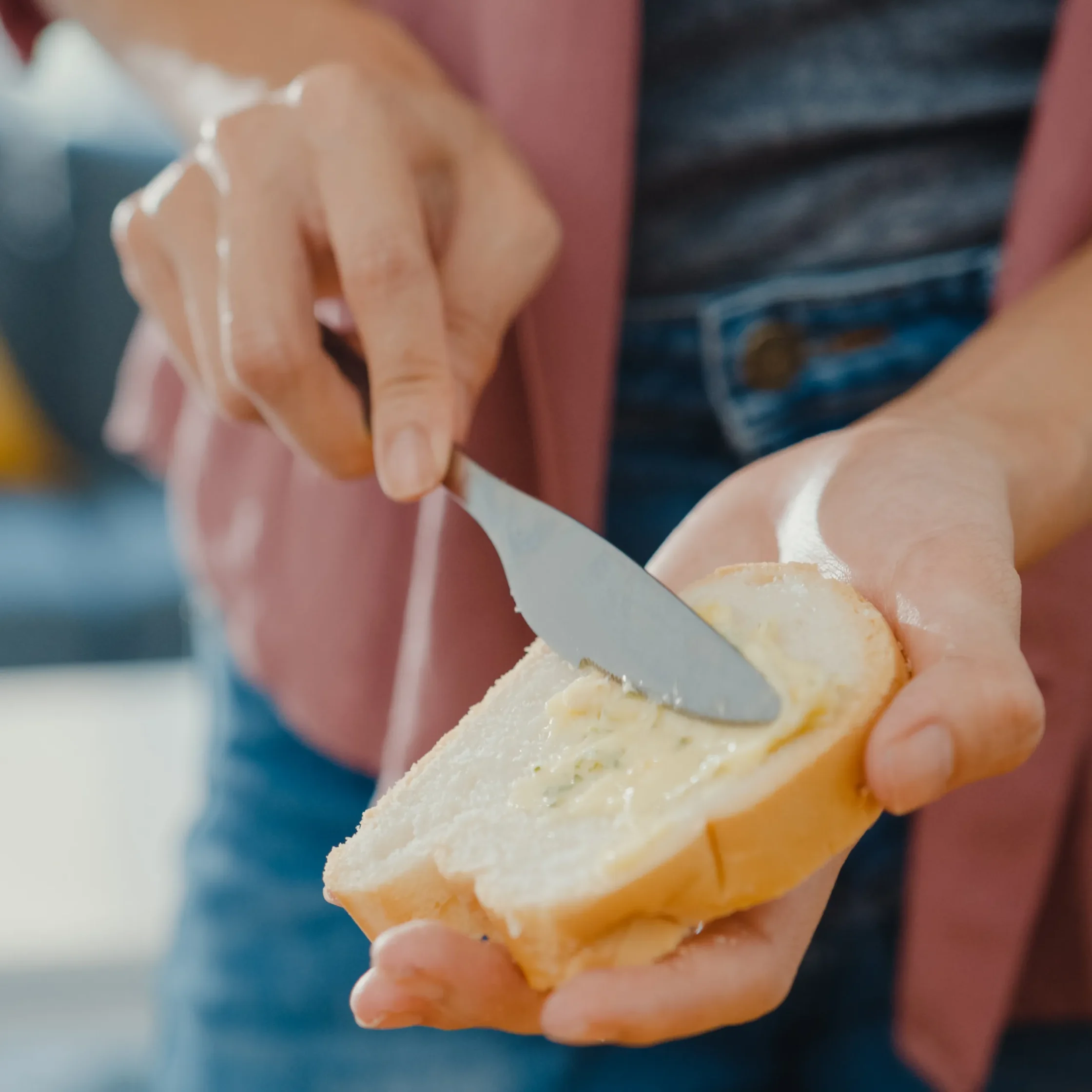 Person holding a crusty baguette while slicing bread with a knife in a kitchen scene