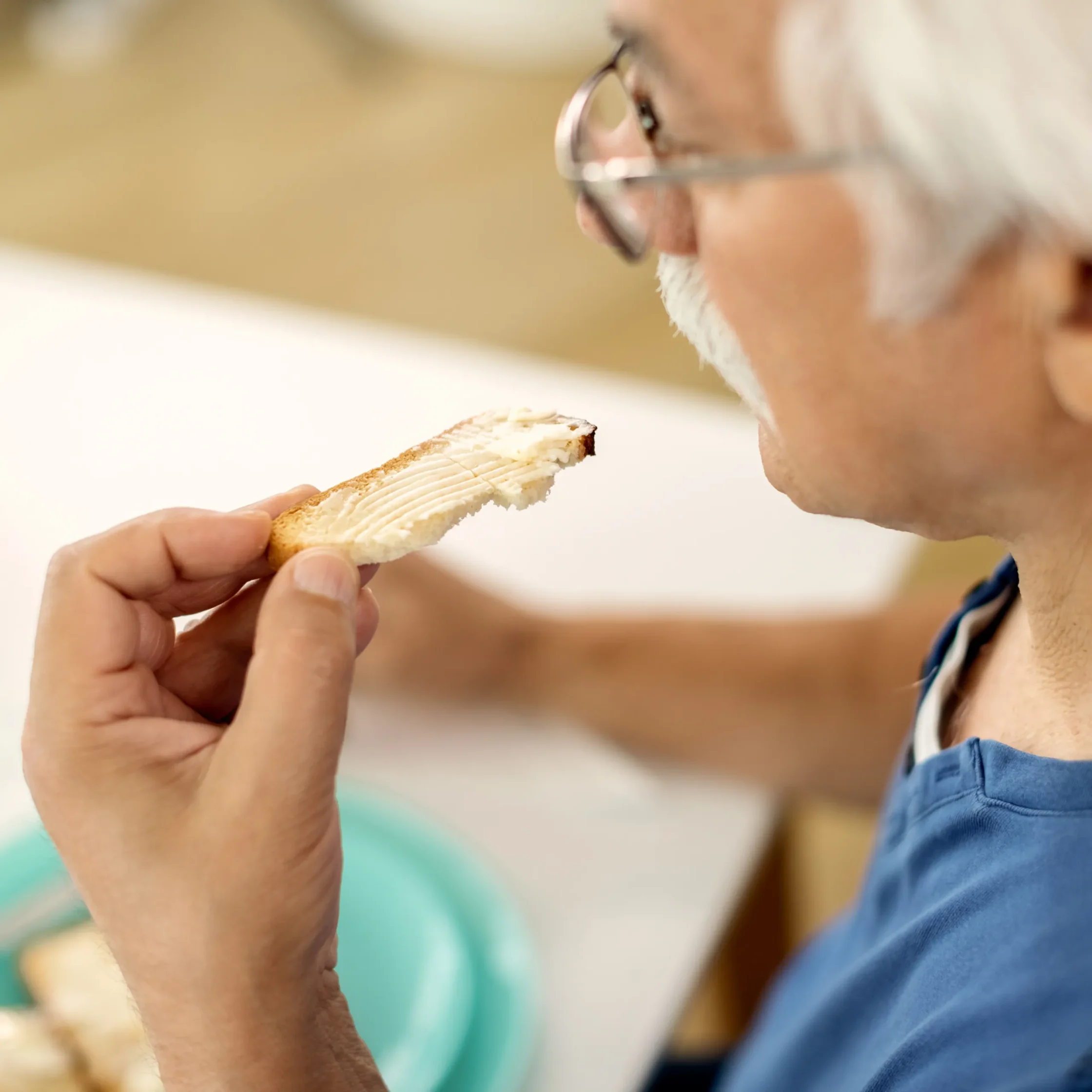 Close-up of an older man with glasses taking a bite of a slice of toasted bread.