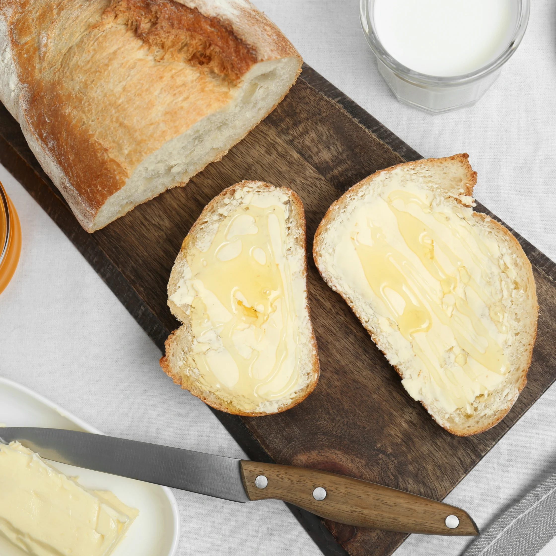 Slices of buttered bread on a wooden cutting board with a bread loaf nearby and a knife resting on the board