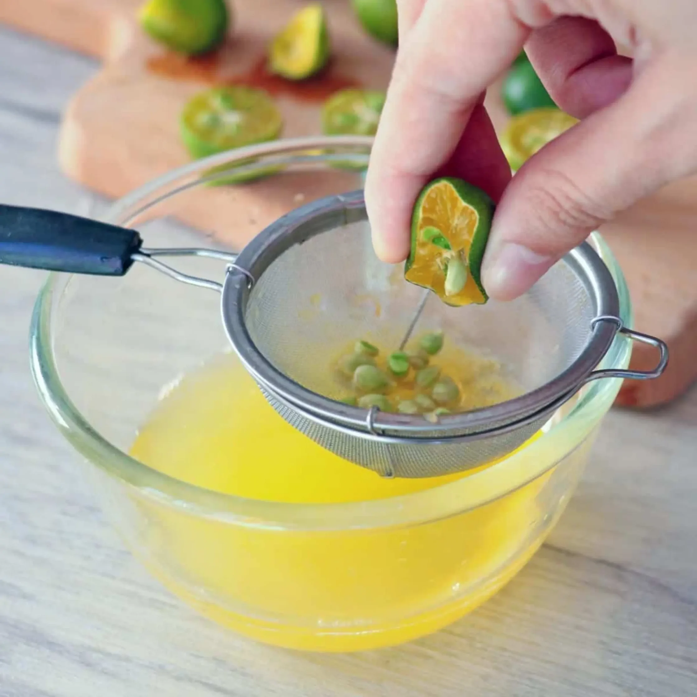 Person squeezing lime halves over a metal juice strainer attached to a yellow juicer, mid-action pulp and juice visible