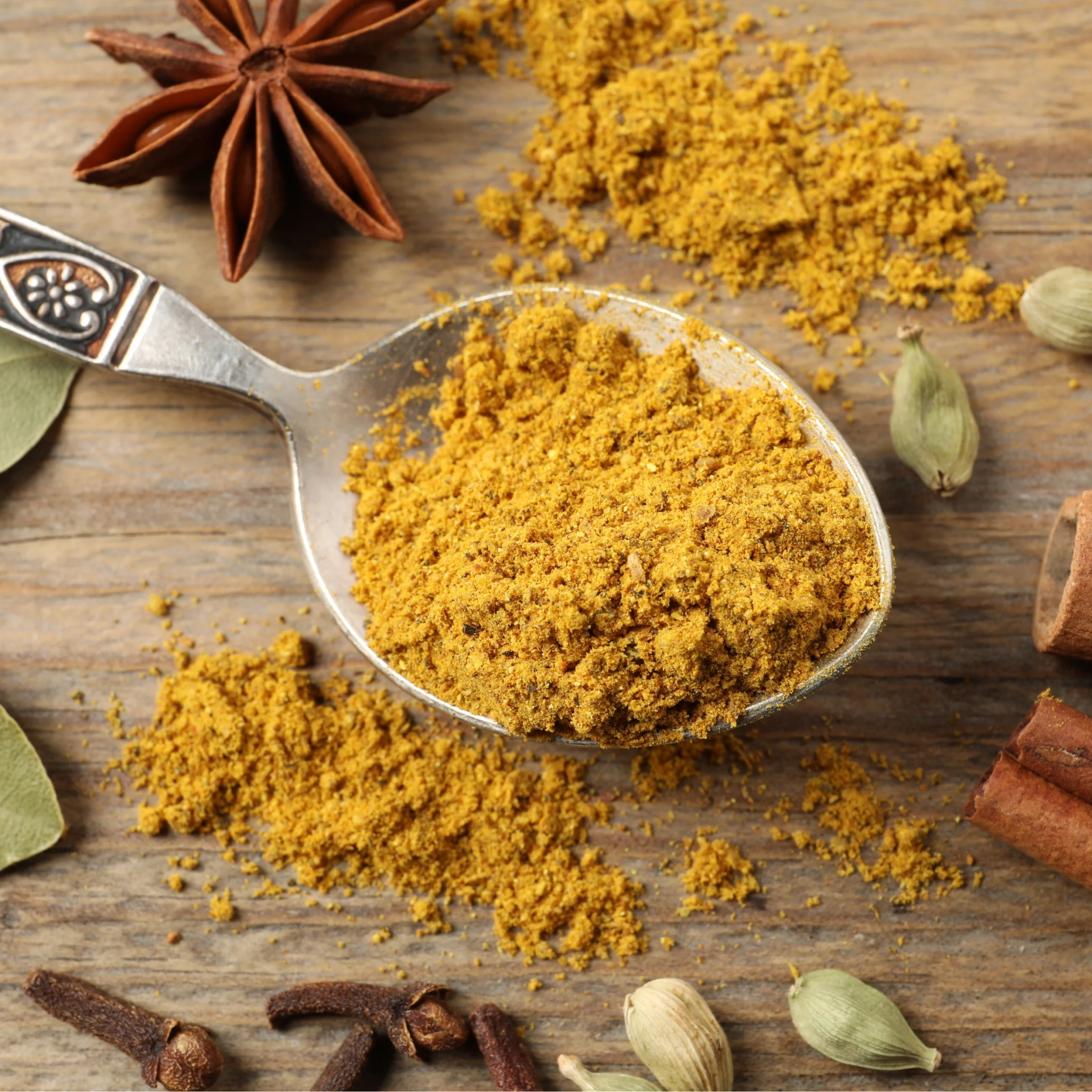 Ground brown spice scattered on a rustic wooden surface with star anise and cardamom pods nearby.