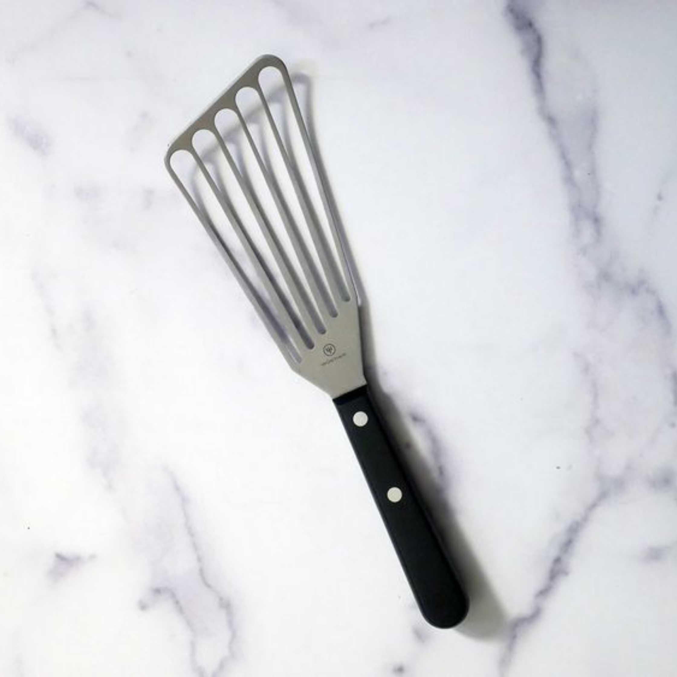 Stainless steel slotted spatula with a black handle on a marble countertop