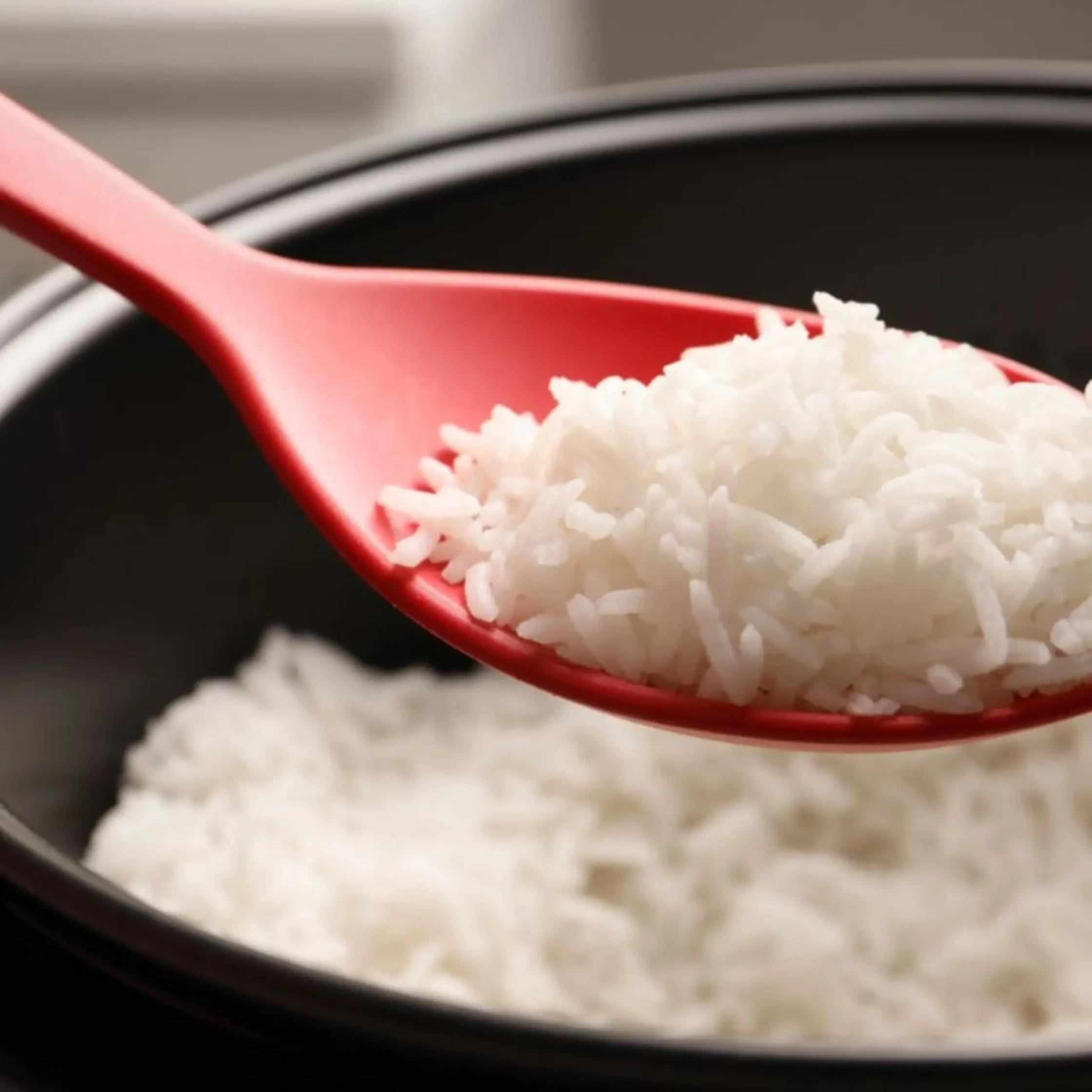 Close-up of white rice grains in a red spoon over a dark background.
