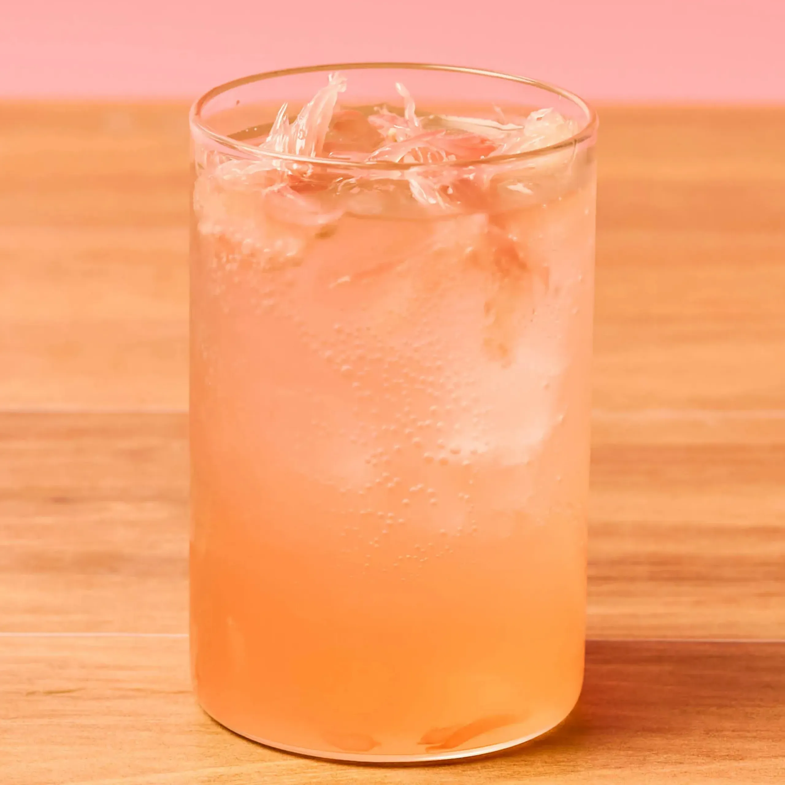 Tall glass of pink-orange iced drink with visible ice cubes on a wooden surface.